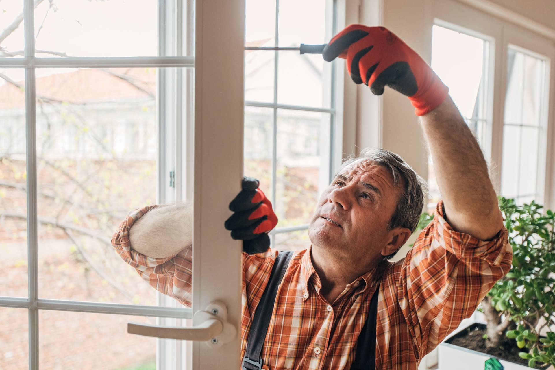 Handwerker in kariertem Hemd repariert ein Fenster mit Schraubendreher