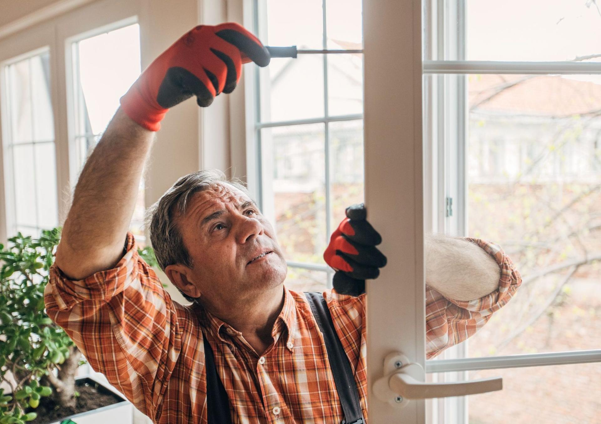 Ein Handwerker repariert ein Fenster mit einem Schraubenzieher in der Hand.