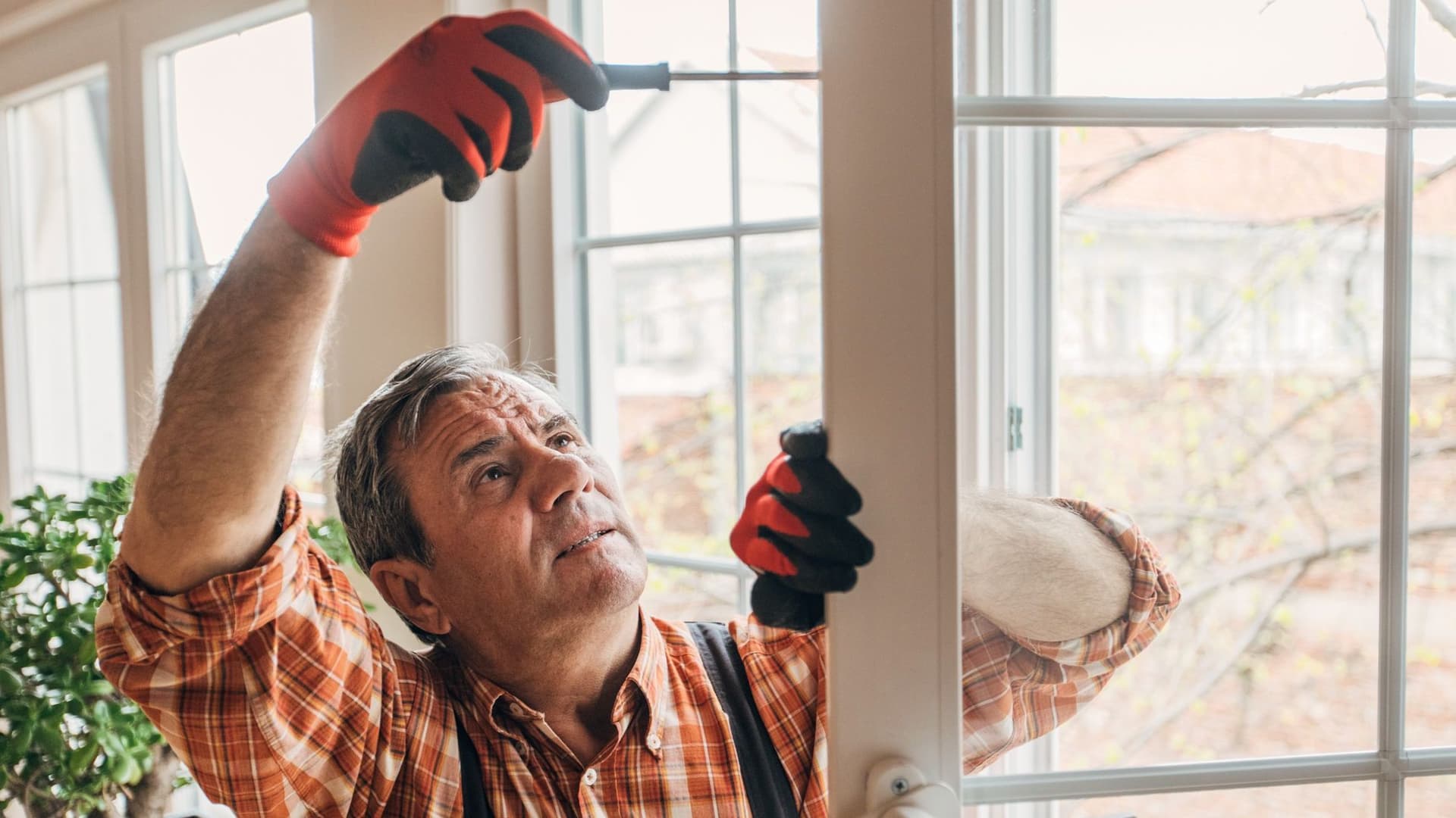 Ein Handwerker repariert ein Fenster mit einem Schraubenzieher in der Hand.