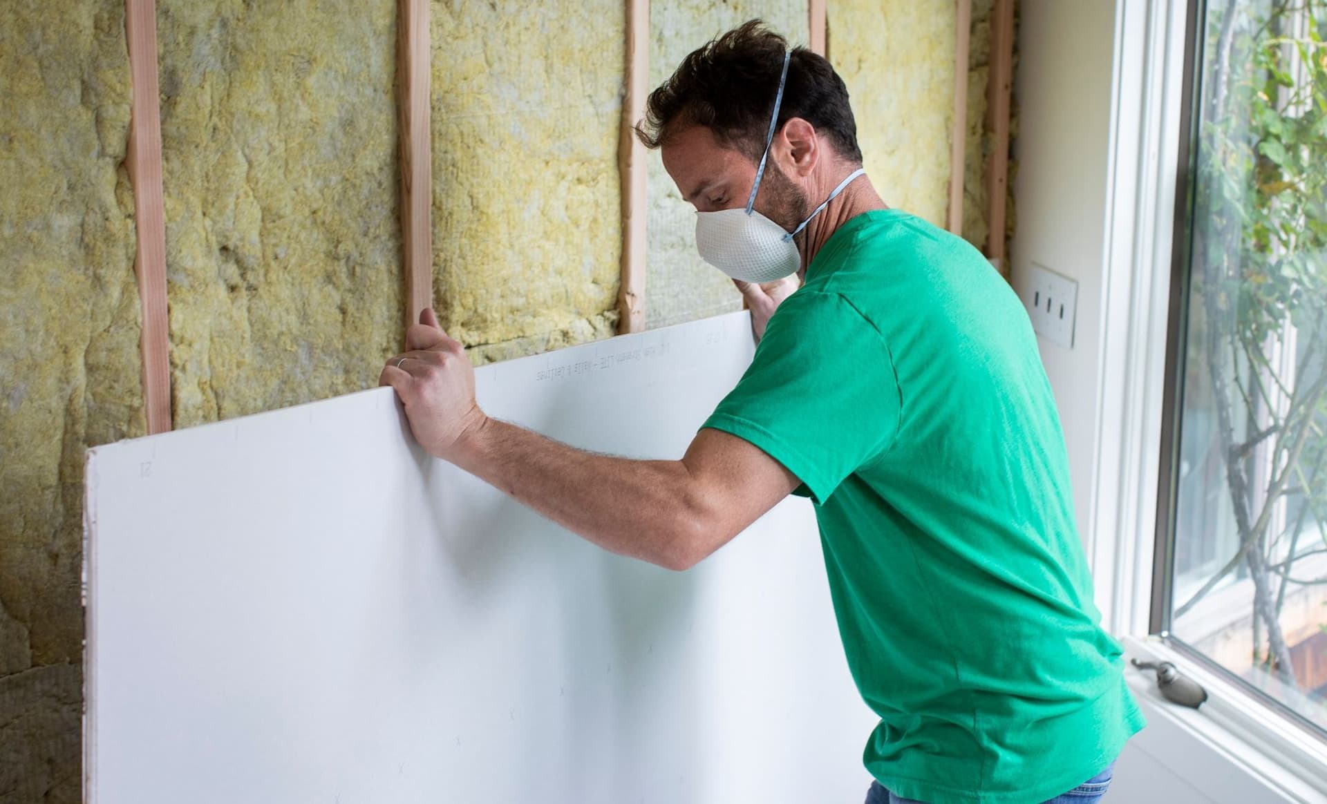 Ein Mann installiert auf der Baustelle eines Privathauses eine Trockenbauwand vor eine Innenwanddämmung. 