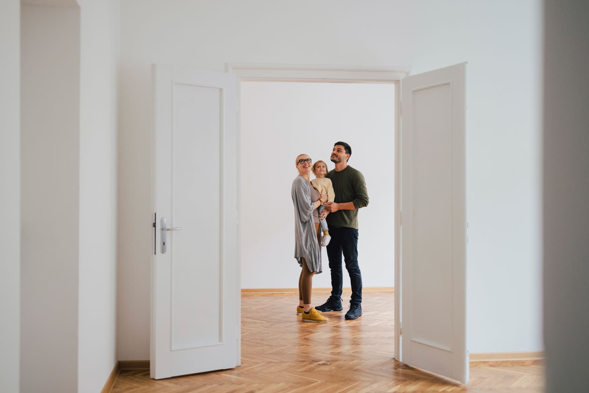 Ein Paar mit Kind steht in einer leeren Wohnung und schaut sich um.