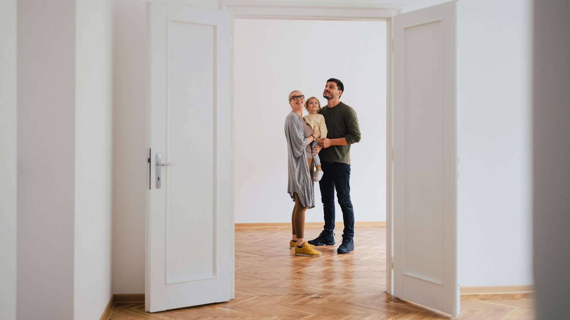Ein Paar mit Kind steht in einer leeren Wohnung und schaut sich um.