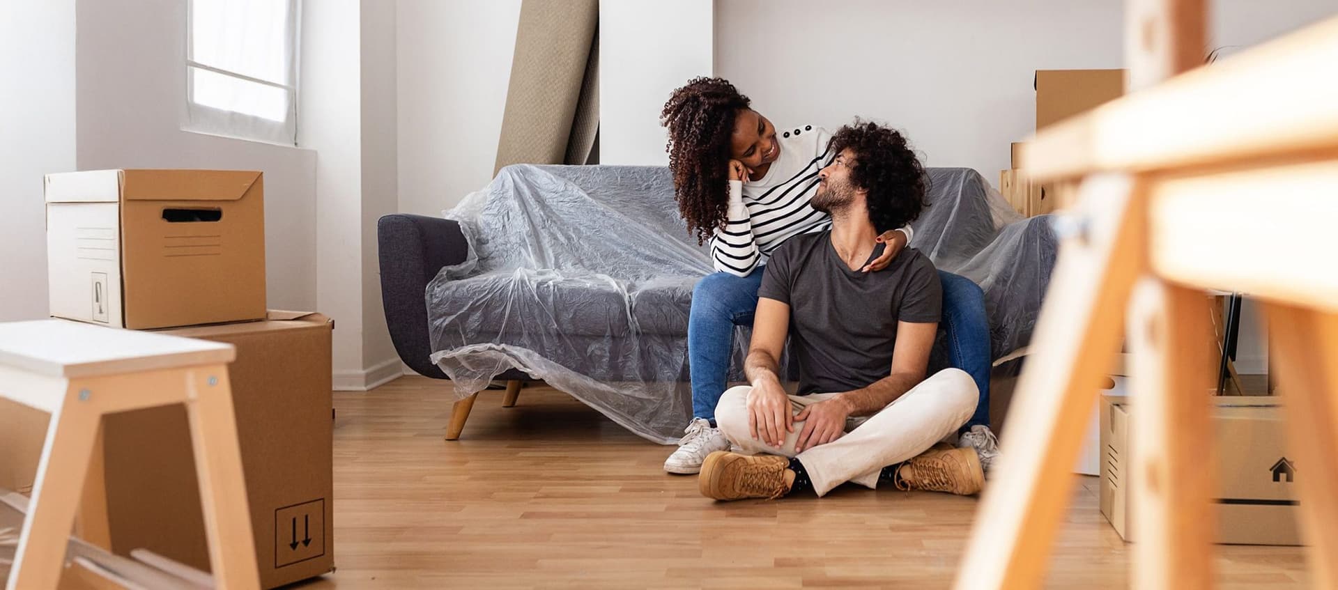 Ein Paar sitzt vor ihrem Sofa neben Umzugskisten in ihrer neuen Wohnung.