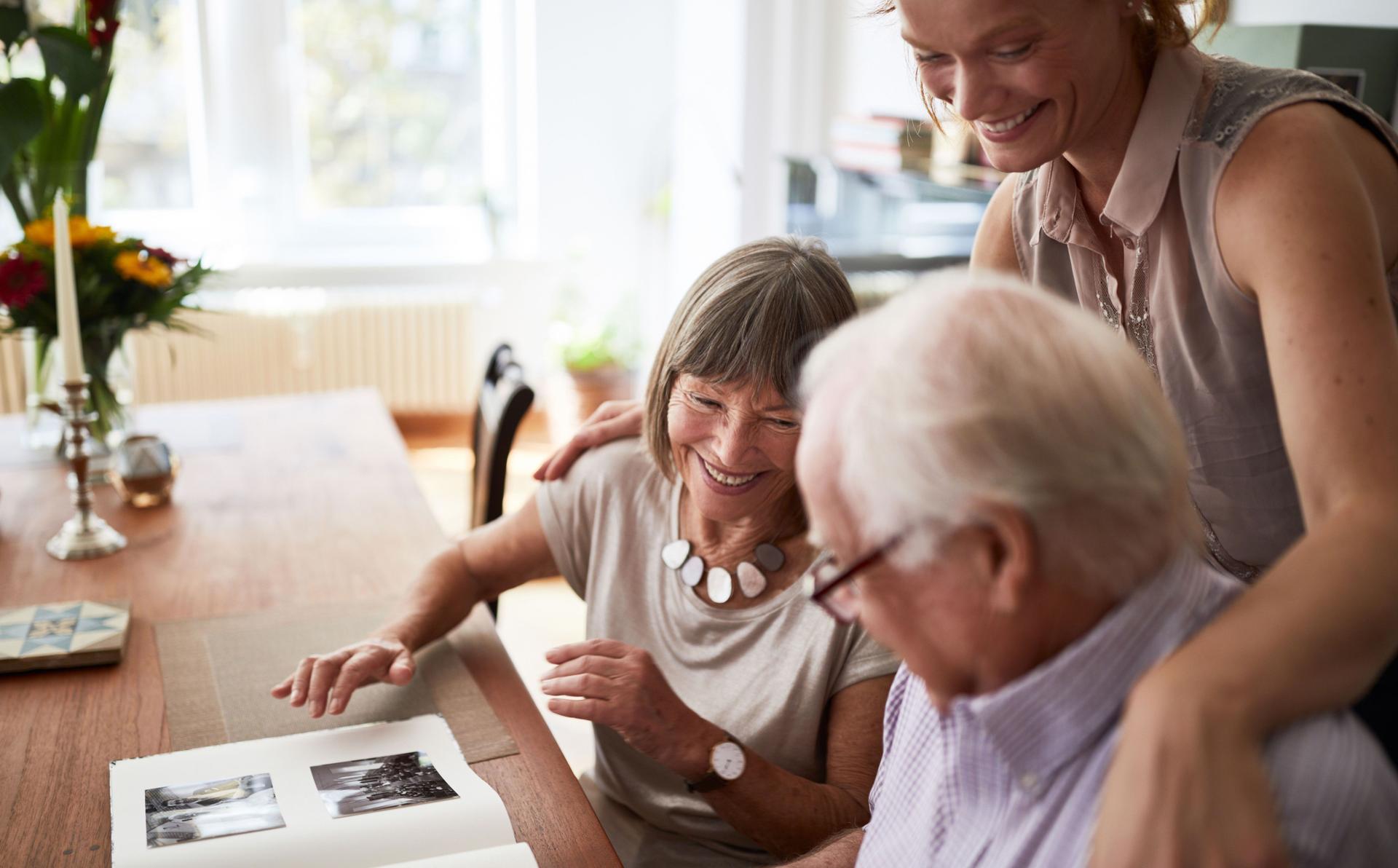 Ein älteres Parr schaut lachend mit einer jungen Frau ein Fotoalbum an.