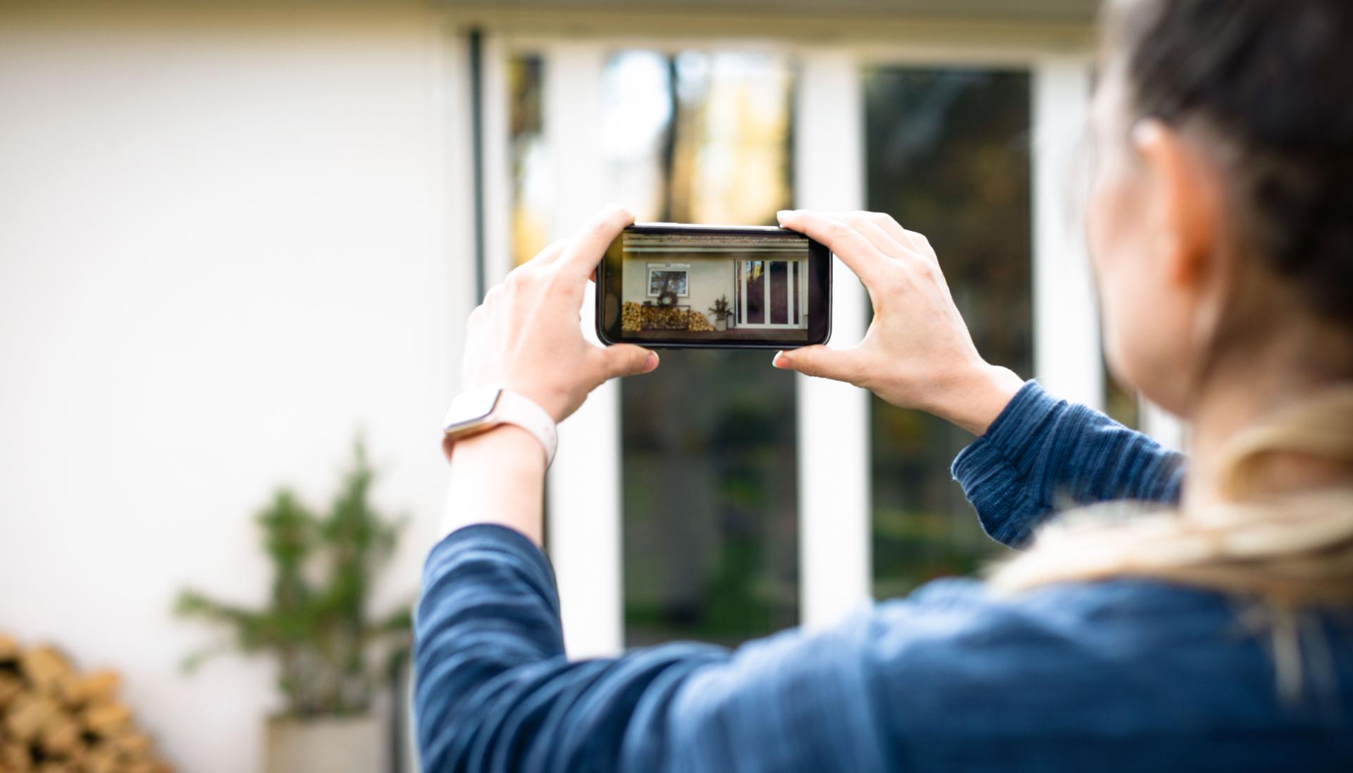 Eine Frau macht mit einem Smartphone ein Bild von einem Haus.
