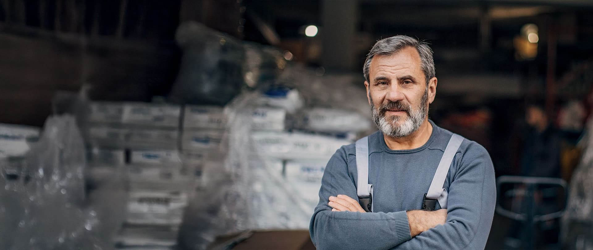 Lagerarbeiter steht mit verschränkten Armen in einer Fabrikhalle.