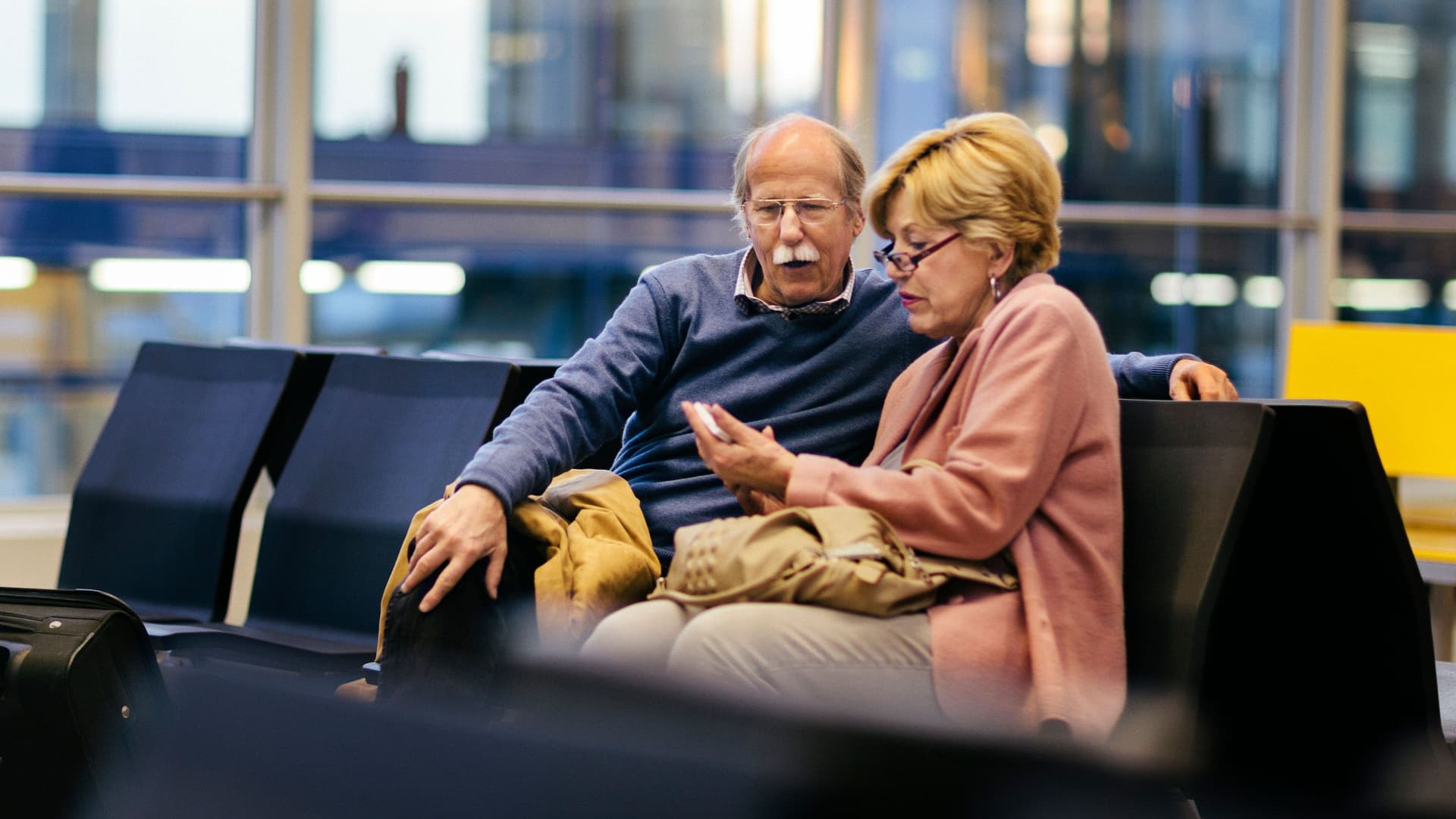 Ein älteres Paar benutzt ein Smartphone, während es am Flughafen wartet