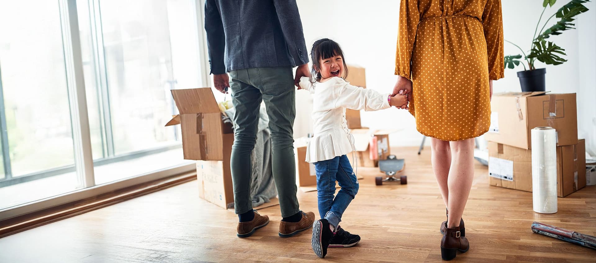 Familie mit Kind zieht in neue Wohnung ein, Umzugskartons und Pflanzen im Hintergrund