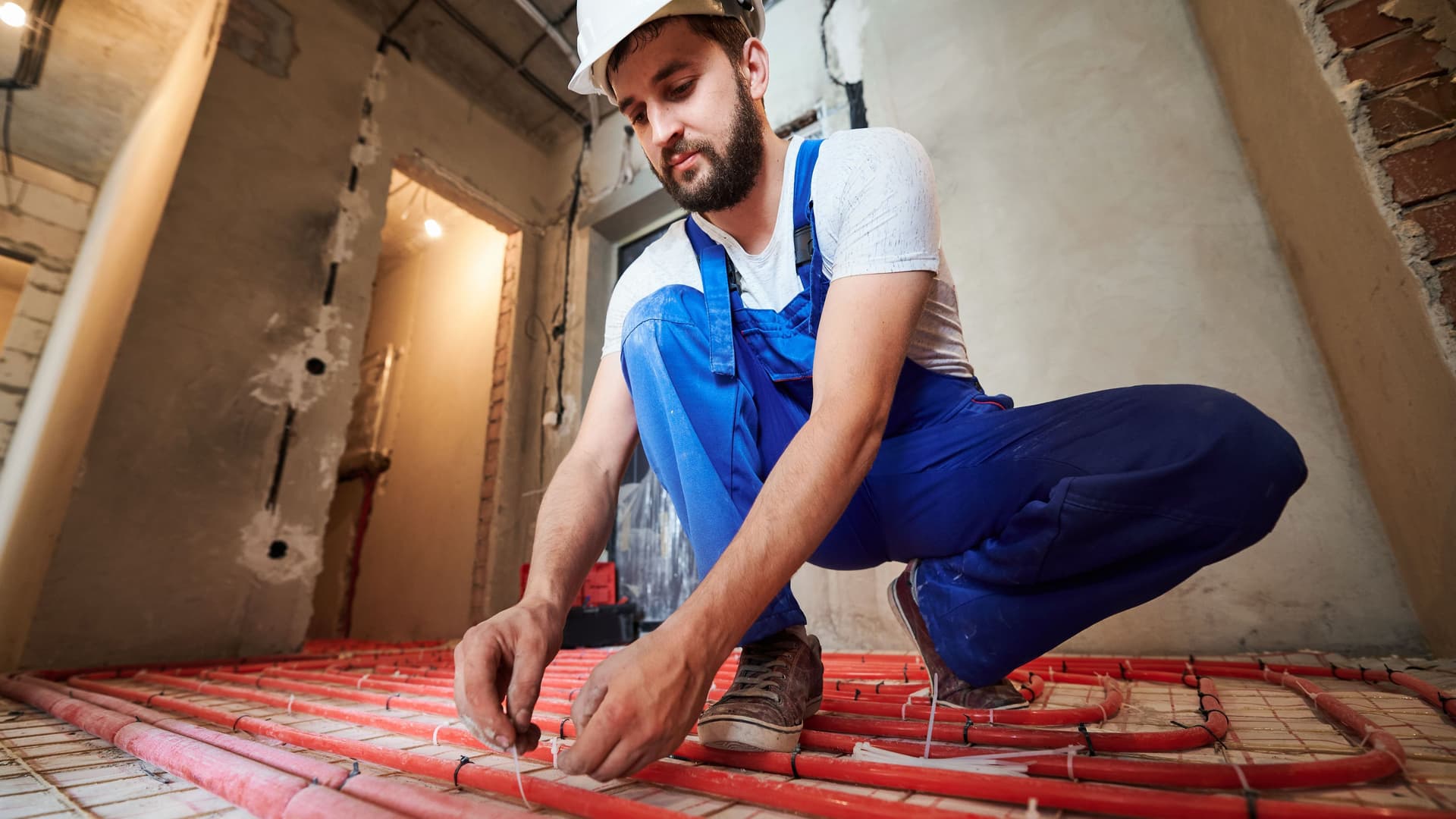 Ein Handwerker verlegt auf einer Baustelle die Bodenheizung.