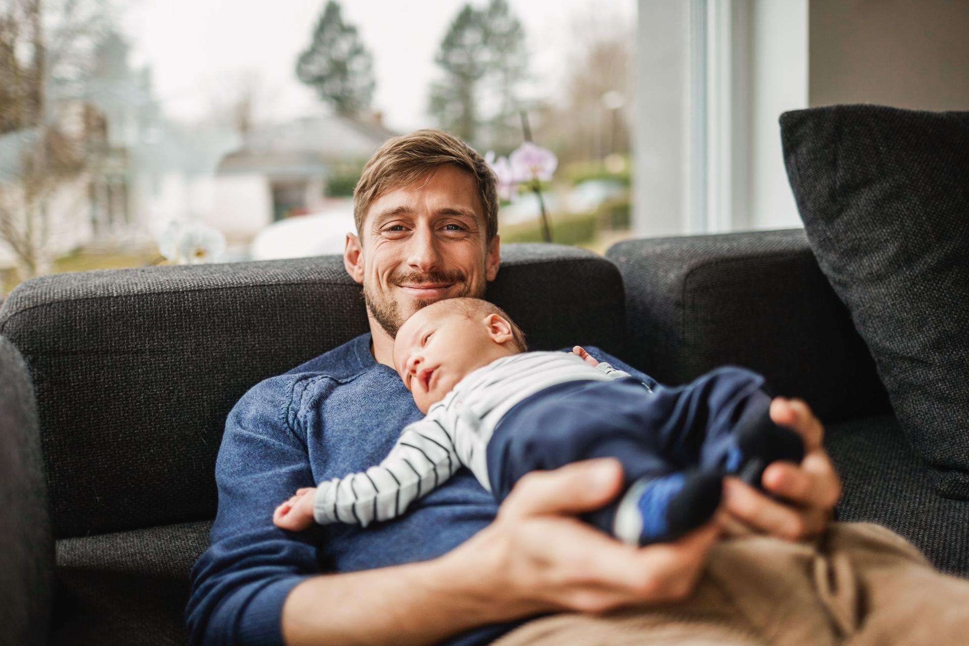 Ein Mann sitzt mit seinem Baby glücklich in seinem Haus auf der Couch.