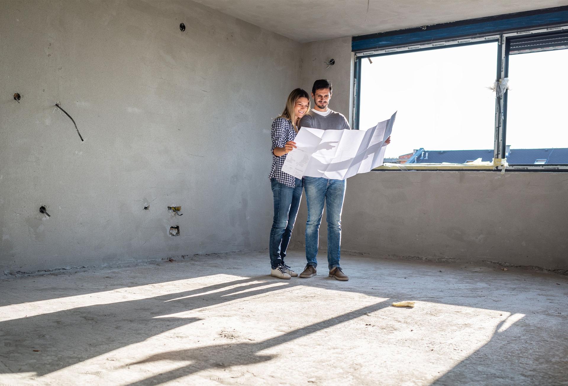 Ein Paar steht mit einem Bauplan in dem Rohbau ihres neuen Hauses.