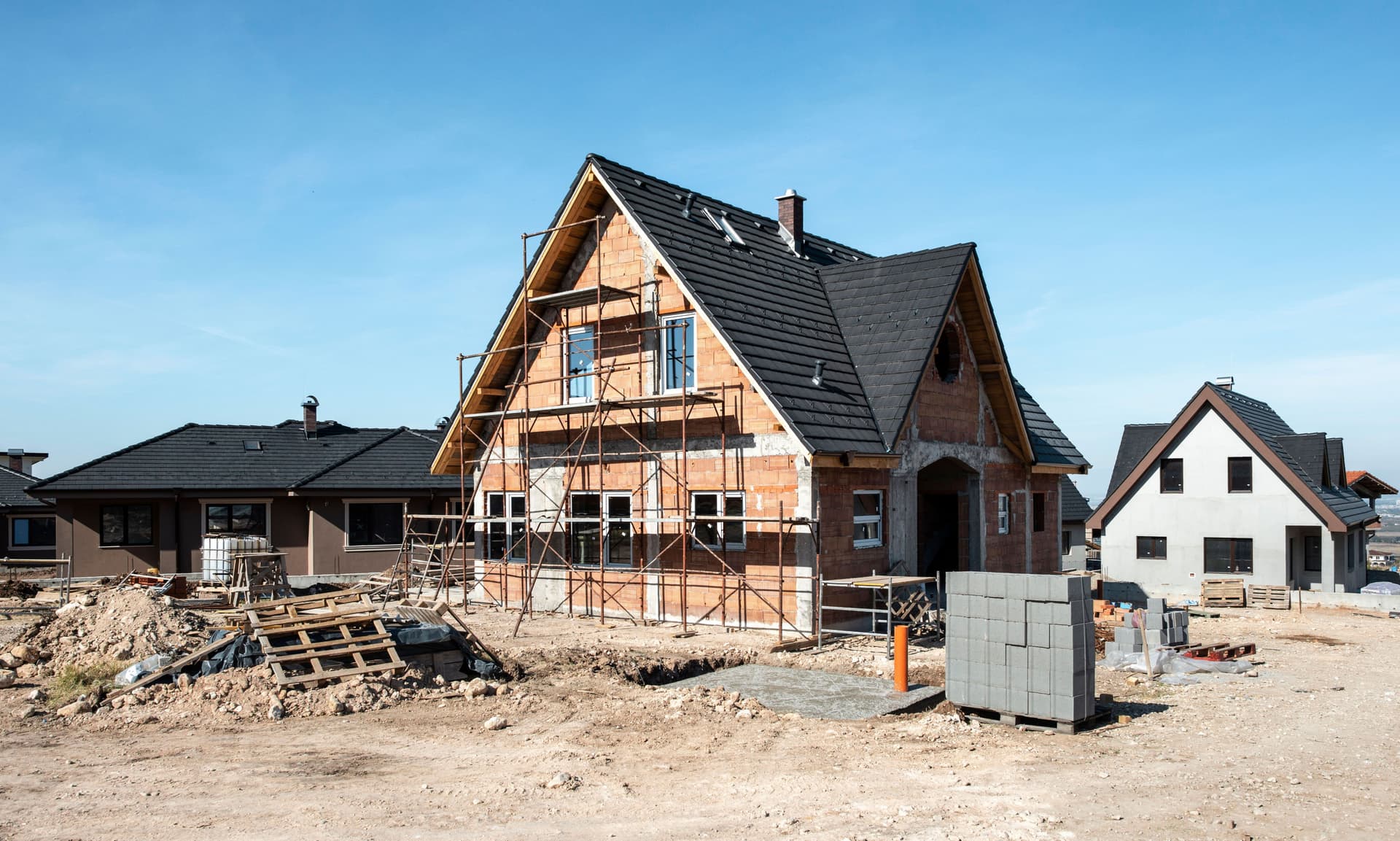 Einfamilienhaus im Rohbau mit Baugerüst und schwarzen Dachziegeln, das erschlossen wird, in einem Neubaugebiet