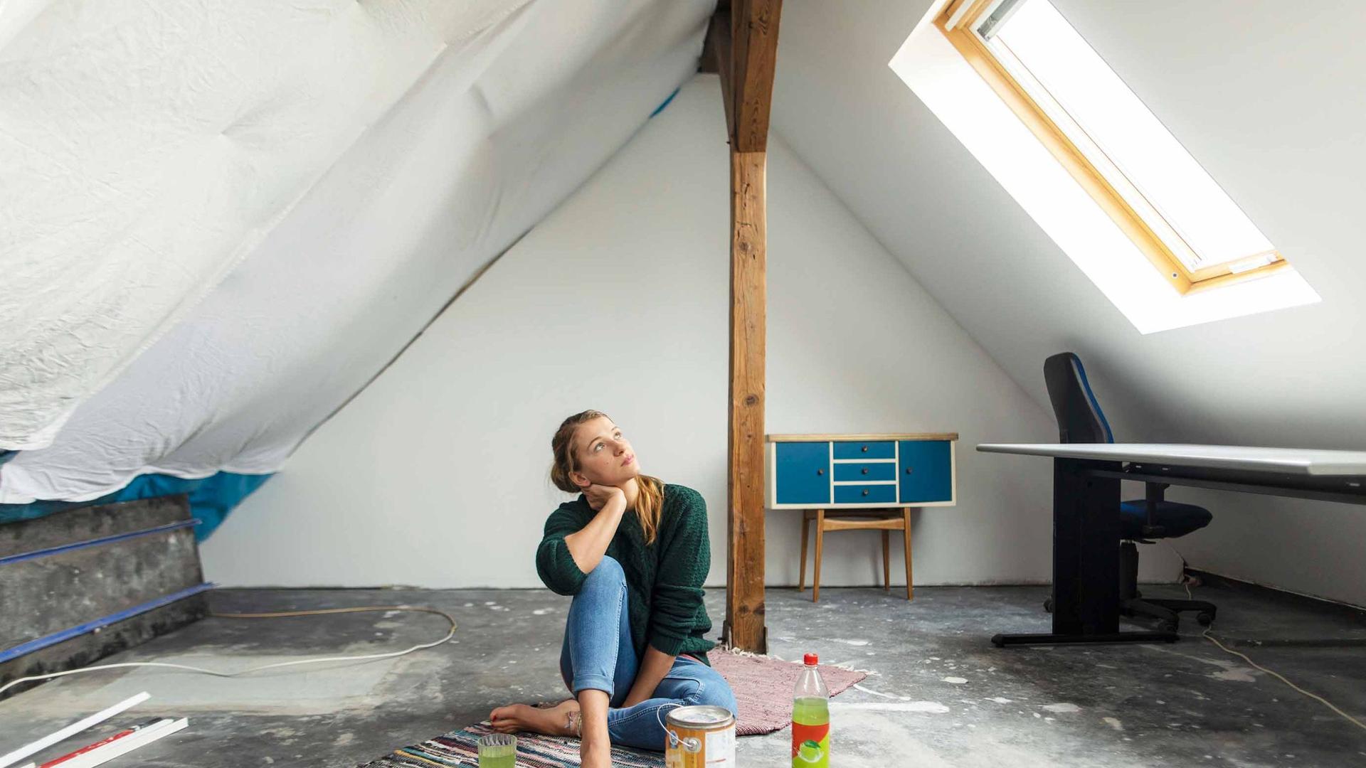 Eine junge Frau sitzt mitten in ihren Renovierungsarbeiten im Dachgeschoss.