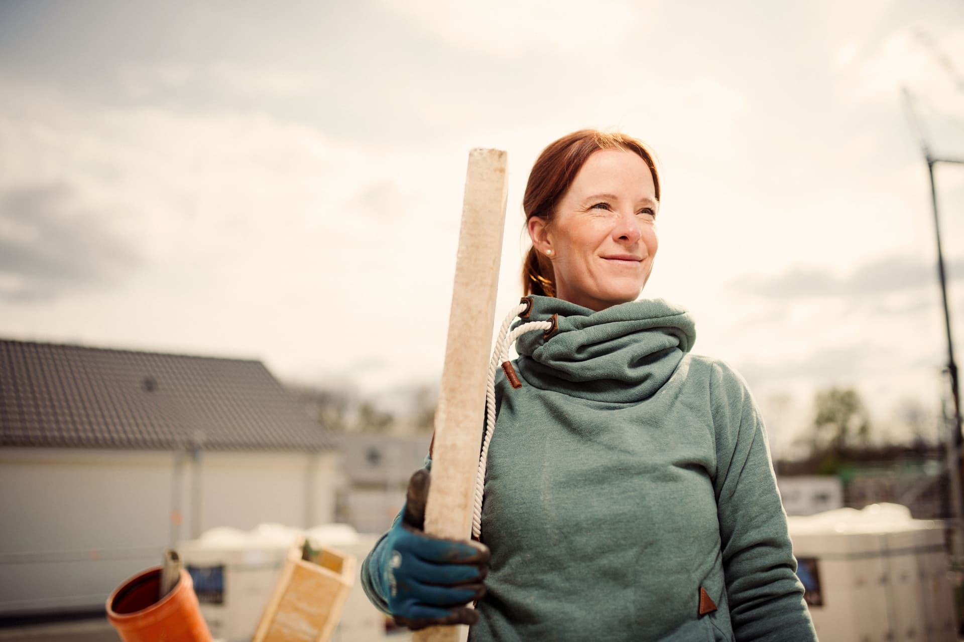 Eine Frau steht mit einem Stück Holz in der Hand auf einer Baustelle.