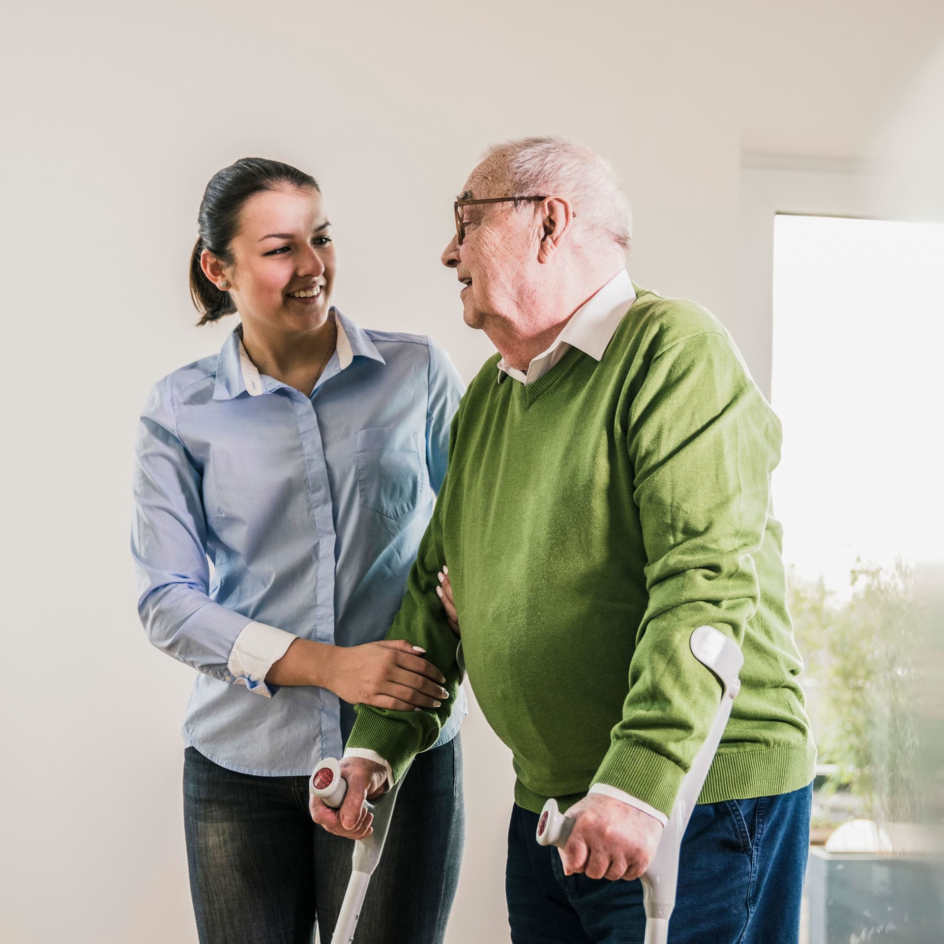 Junge Frau hilft einem älterer Mann auf Krücken.