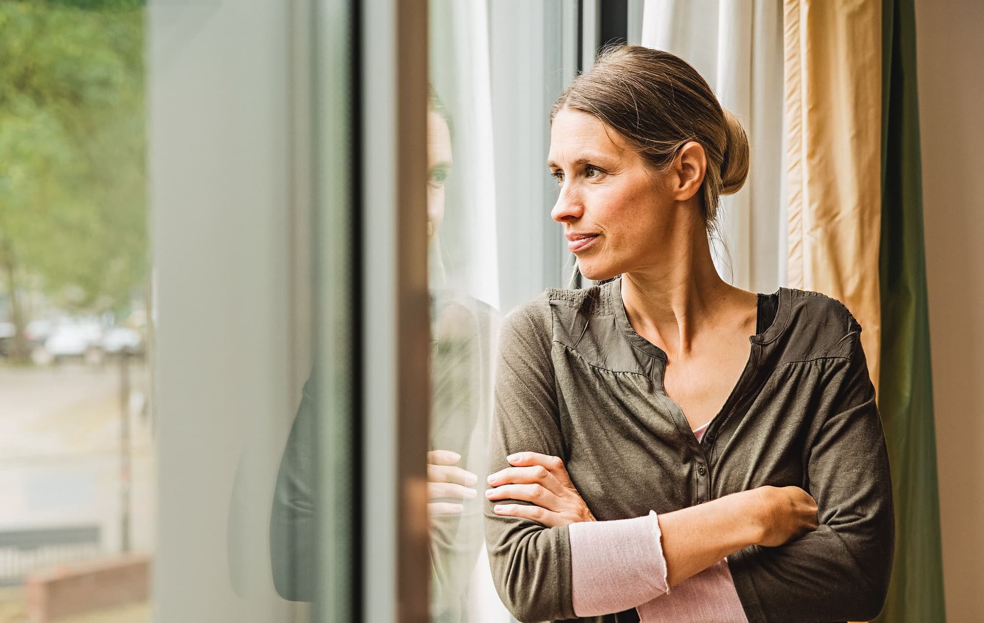 Eine Frau in Gedanken steht an einem Fenster.