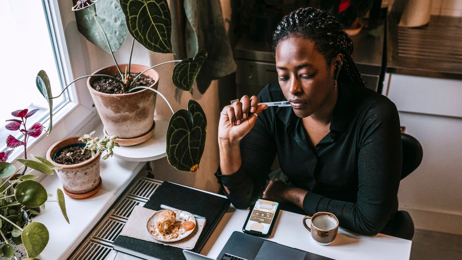 Junge Frau, die mit Laptop in einer Küche sitzt, während sie von zu Hause aus arbeitet.