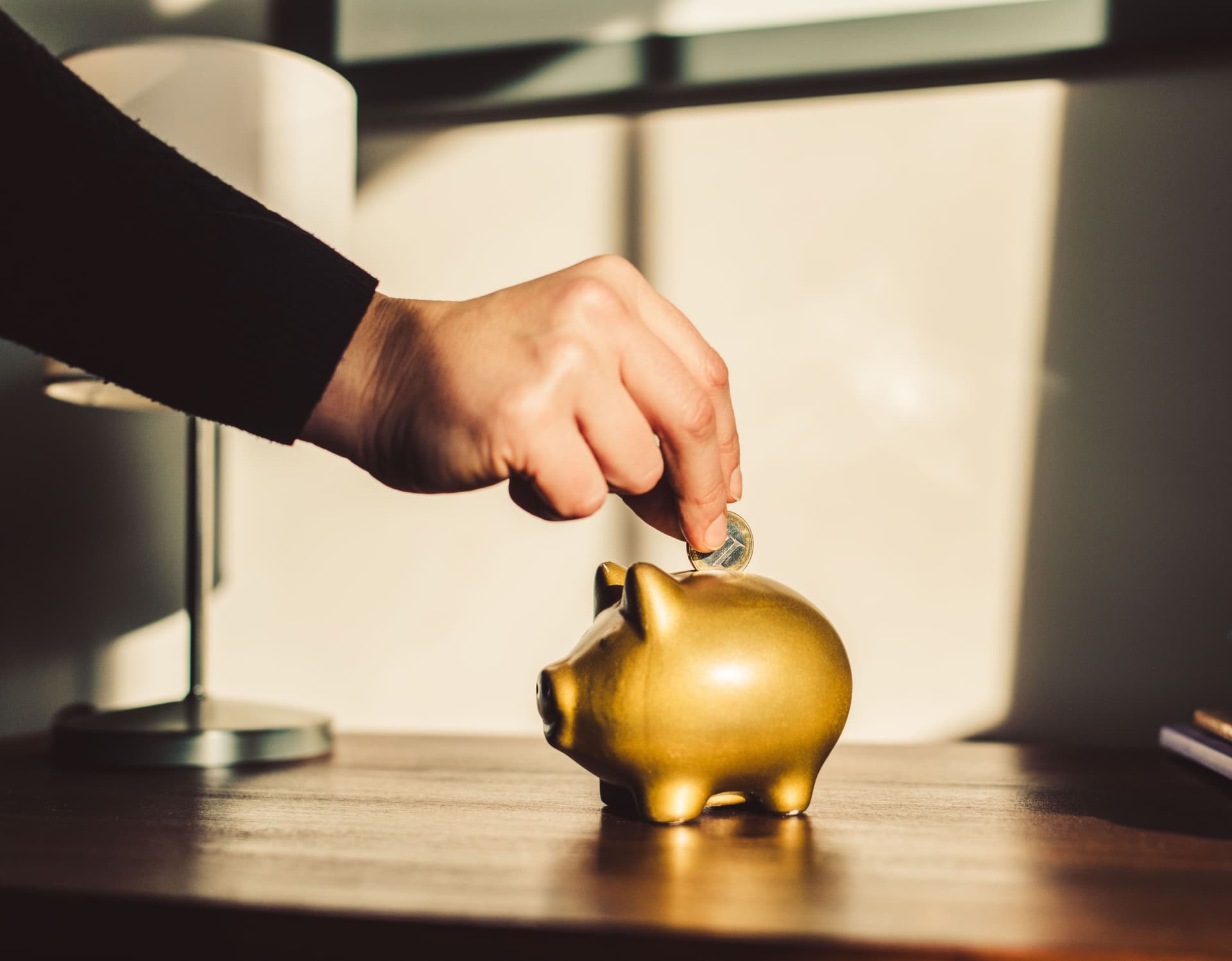 Woman putting coin into a golden piggy bank.