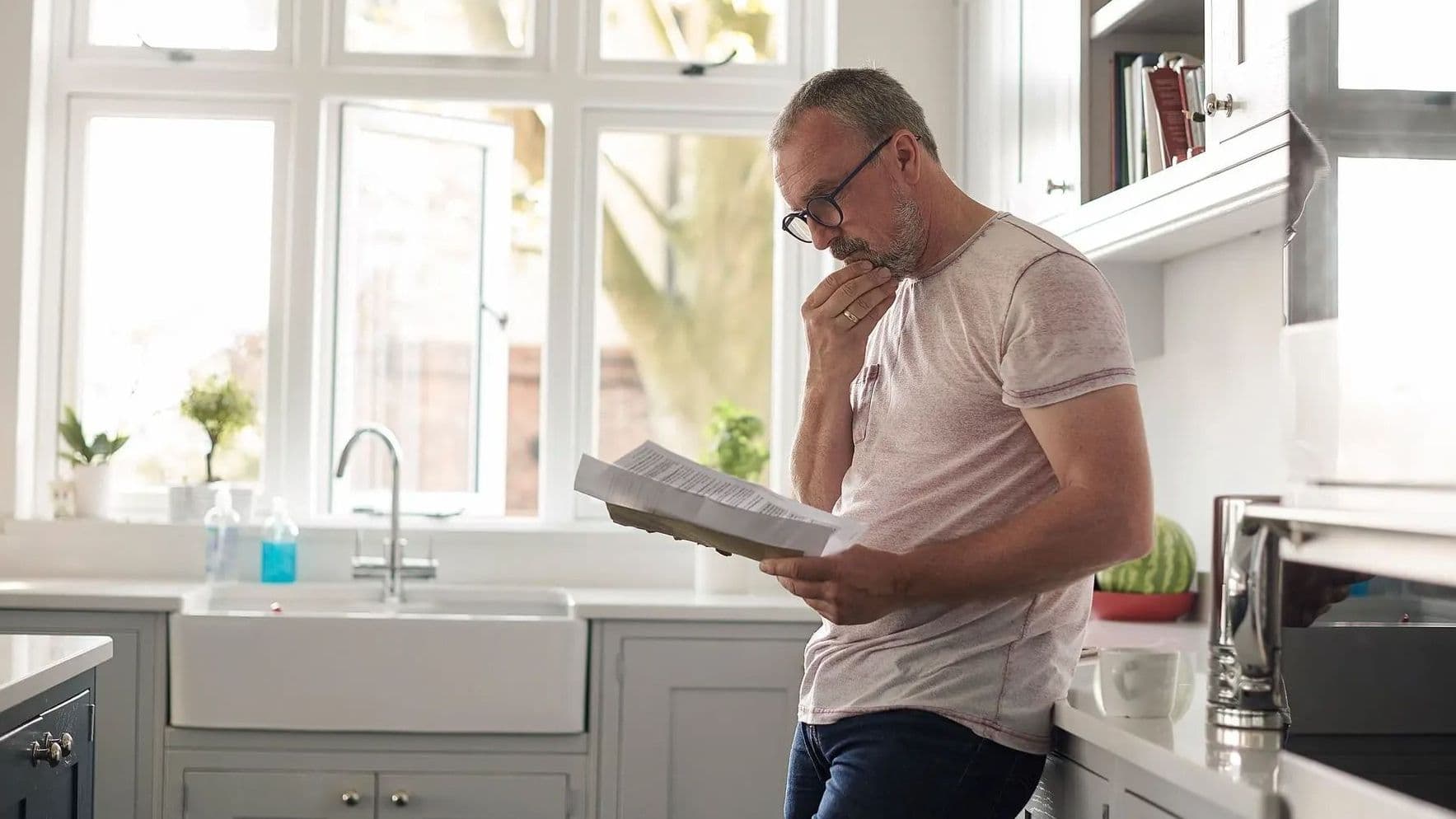 mann mit brille liest nachdenklich ein dokument in moderner küche
