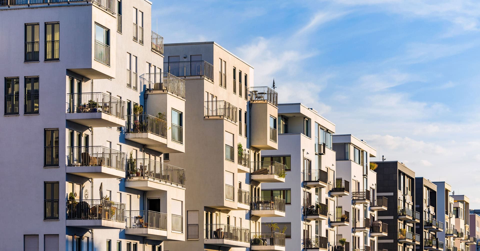 Moderne Wohnhausfassade mit Balkonen und Glasfenstern unter blauem Himmel.