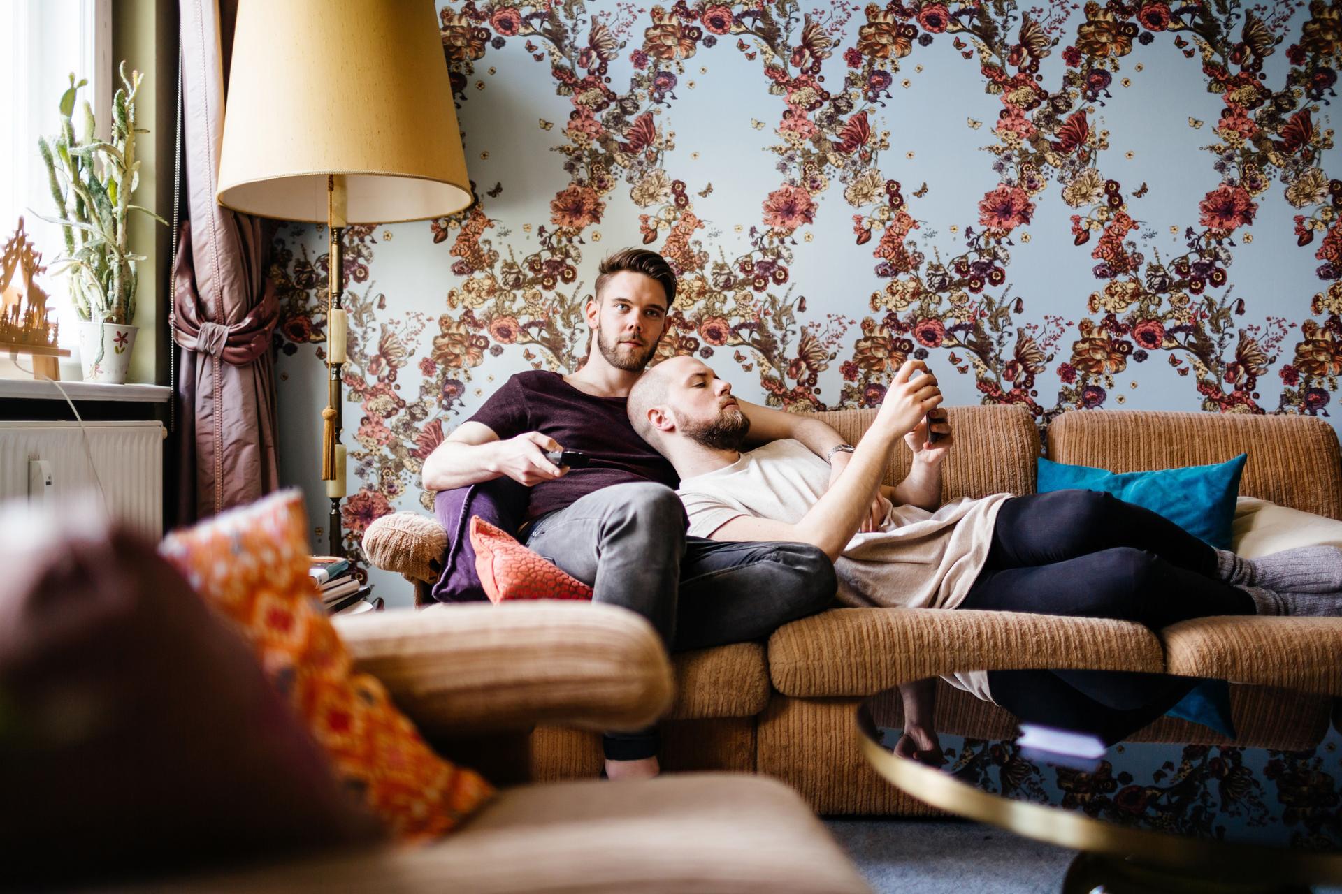Ein männliches Paar sitzt entspannt auf der Couch und schaut Fernsehen.