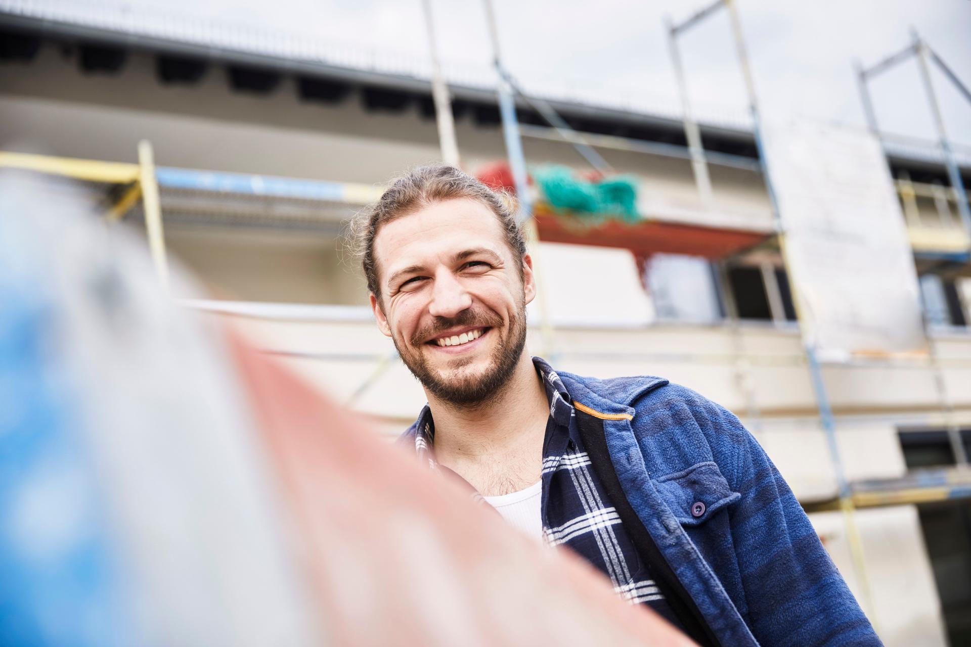 Ein Mann steht lächelnd auf einer Baustelle.