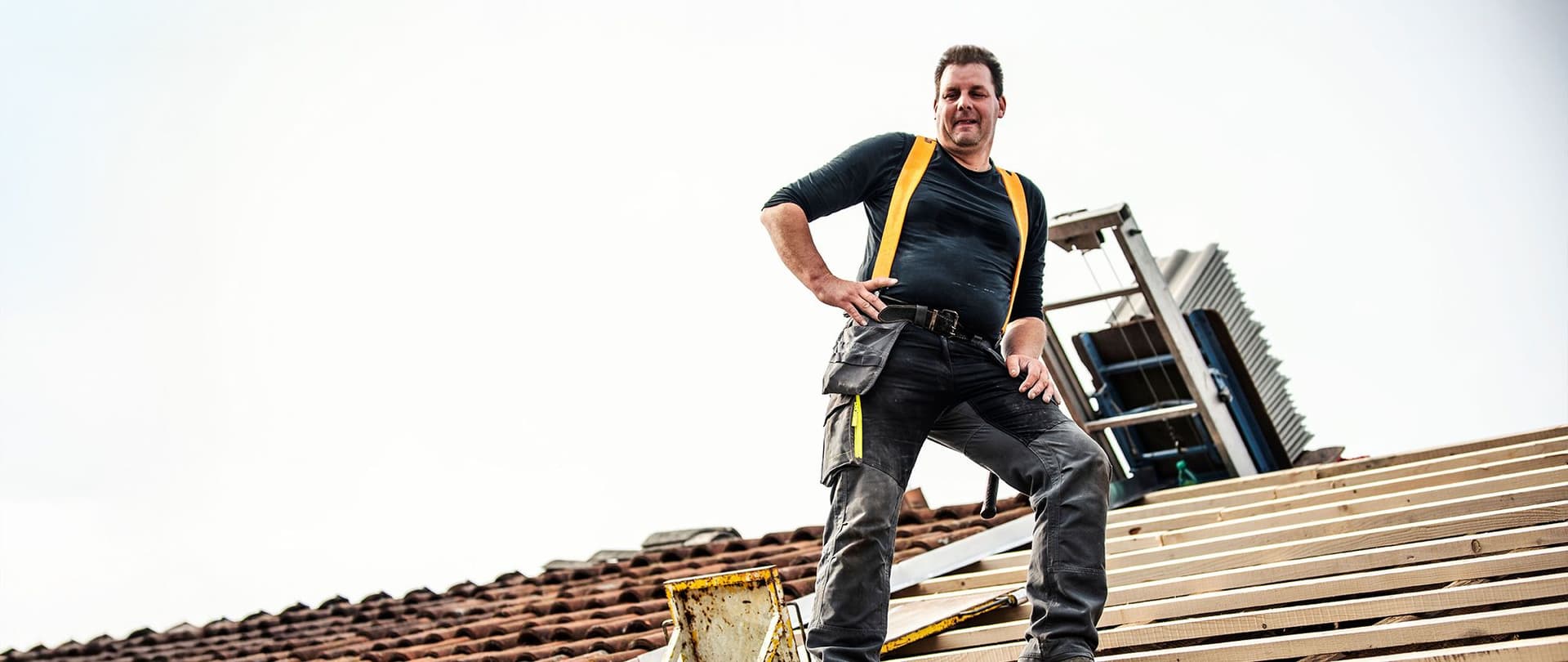 Handwerker mit gelben Hosenträgern steht auf einem Dach und arbeitet an der Dachkonstruktion