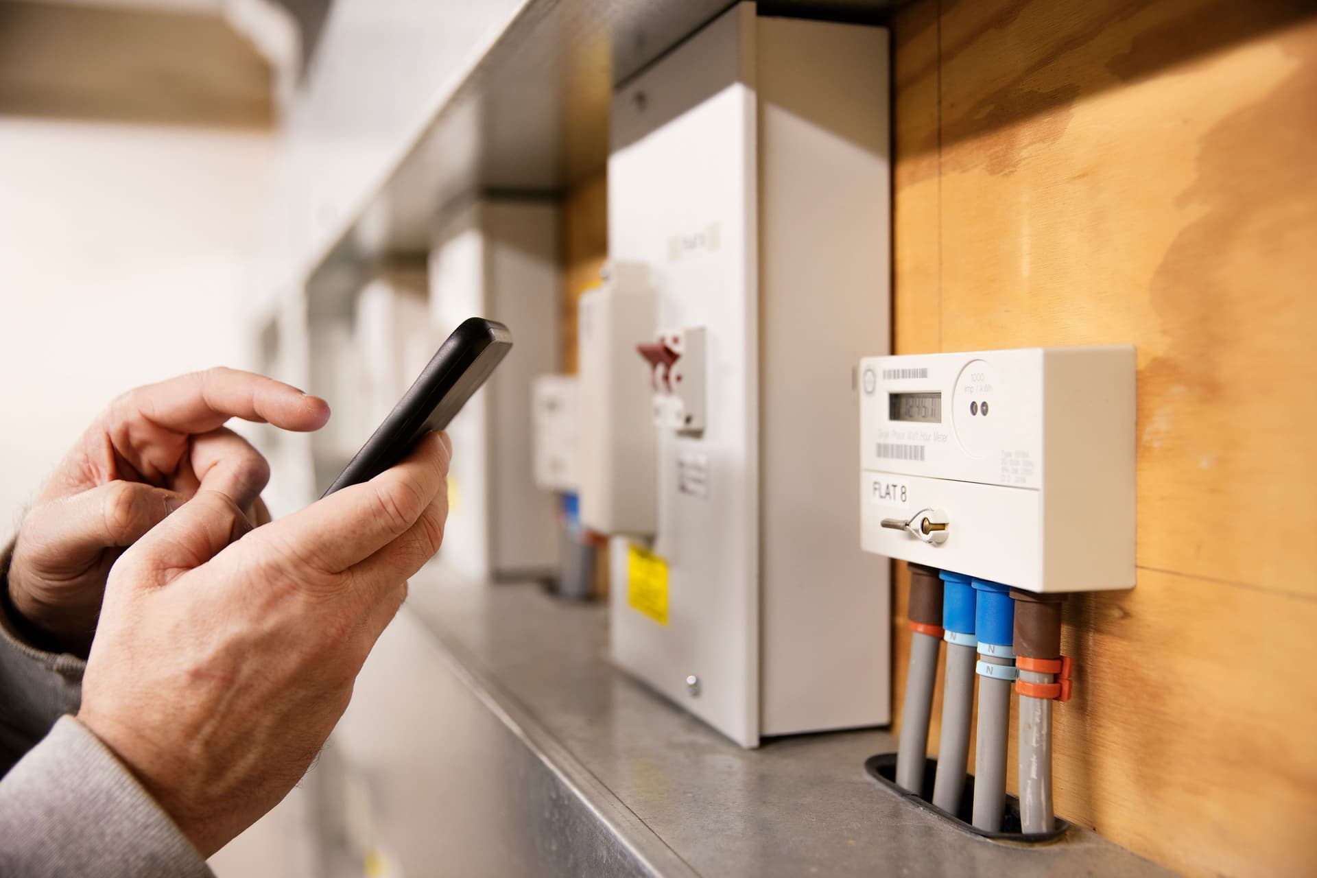 Mann liest mit dem Smartphone den Stromverbrauch am digitalen, smarten Stromzähler ab.