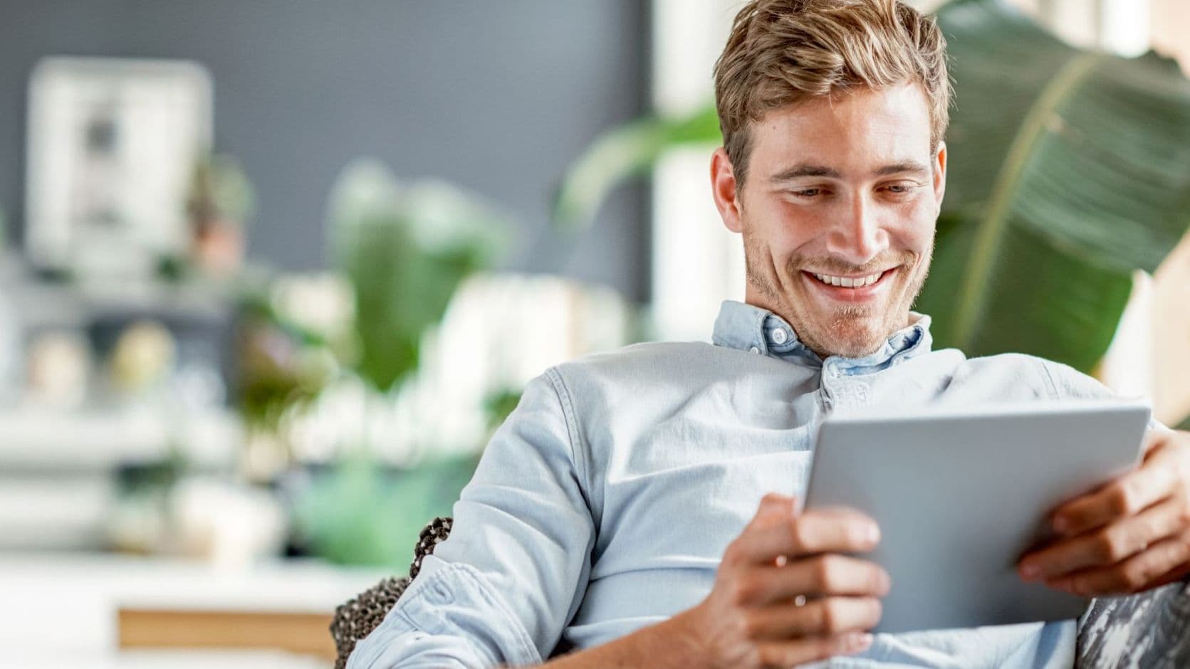Lächelnder Mann auf dem Sofa, der zu Hause auf ein Tablet schaut.
