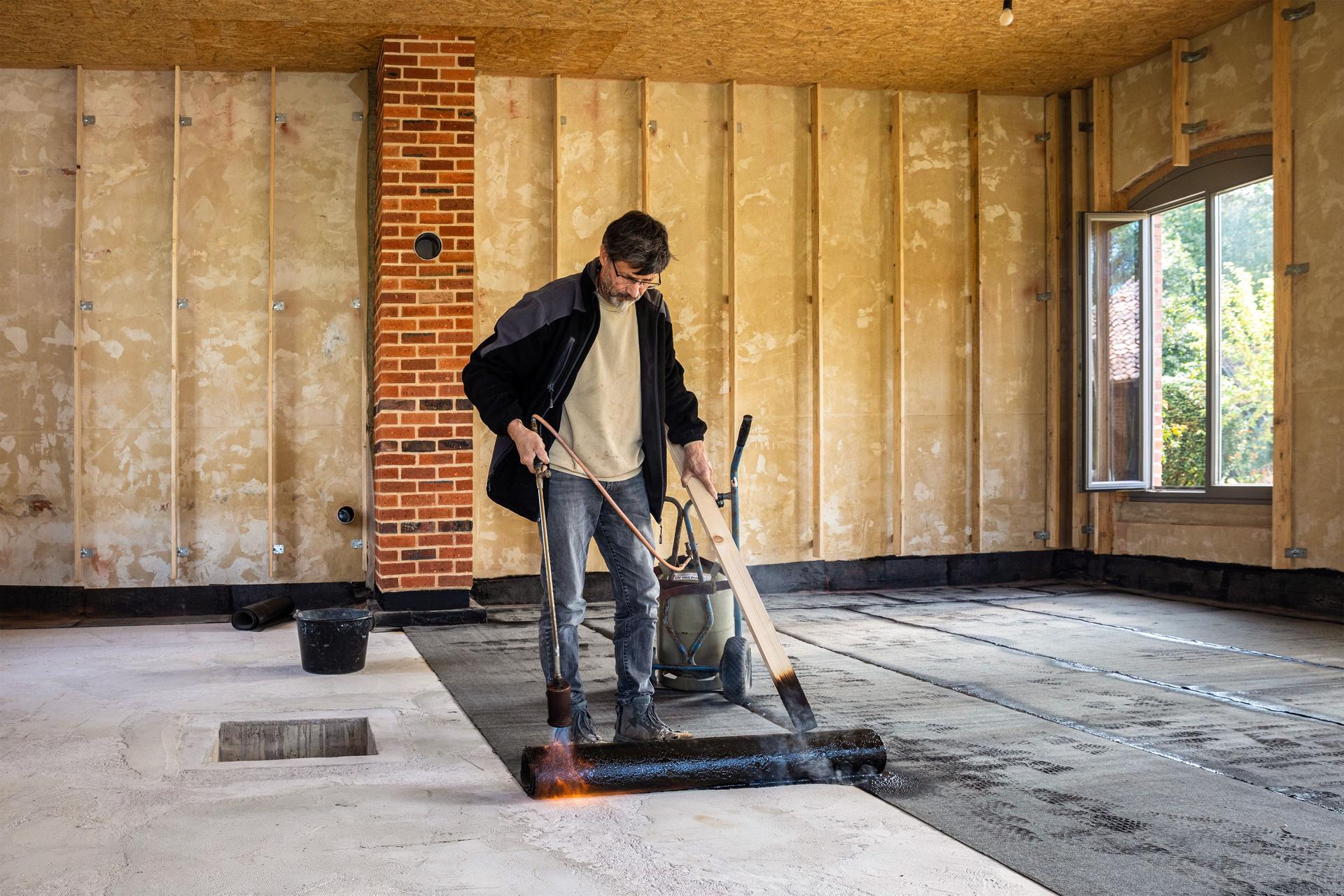 Installation der Abdichtung auf dem Betonfundament durch Erhitzen und Schmelzen von Bitumen-Dachpappenrollen mit einem Propangasbrenner