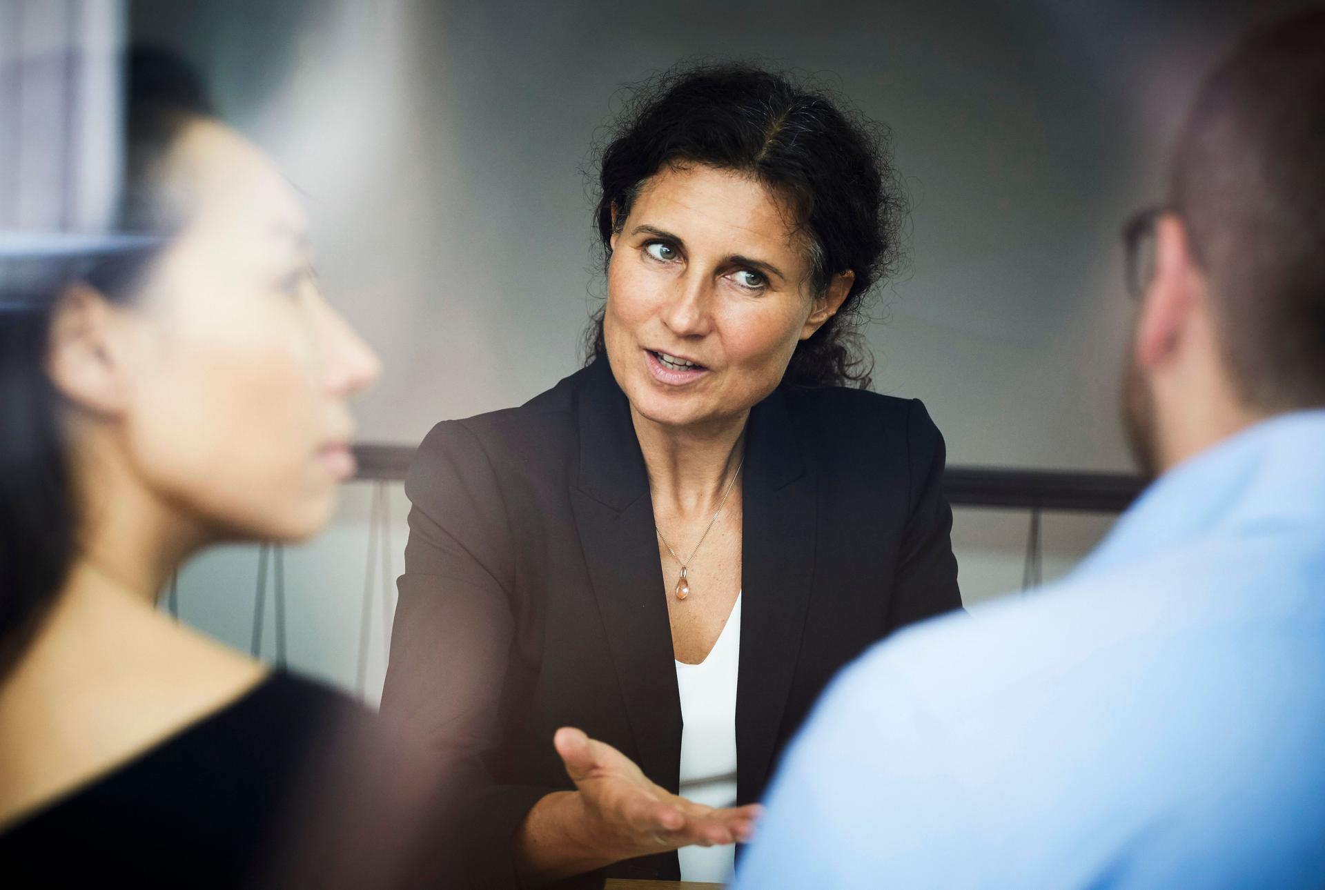 Confident mature female financial advisor discussing with businessman and businesswoman during meeting at office
