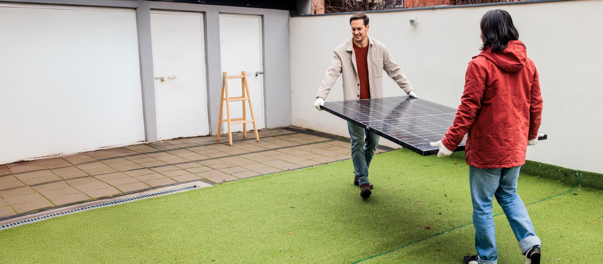 Zwei Personen tragen gemeinsam ein Solarmodul im Freien