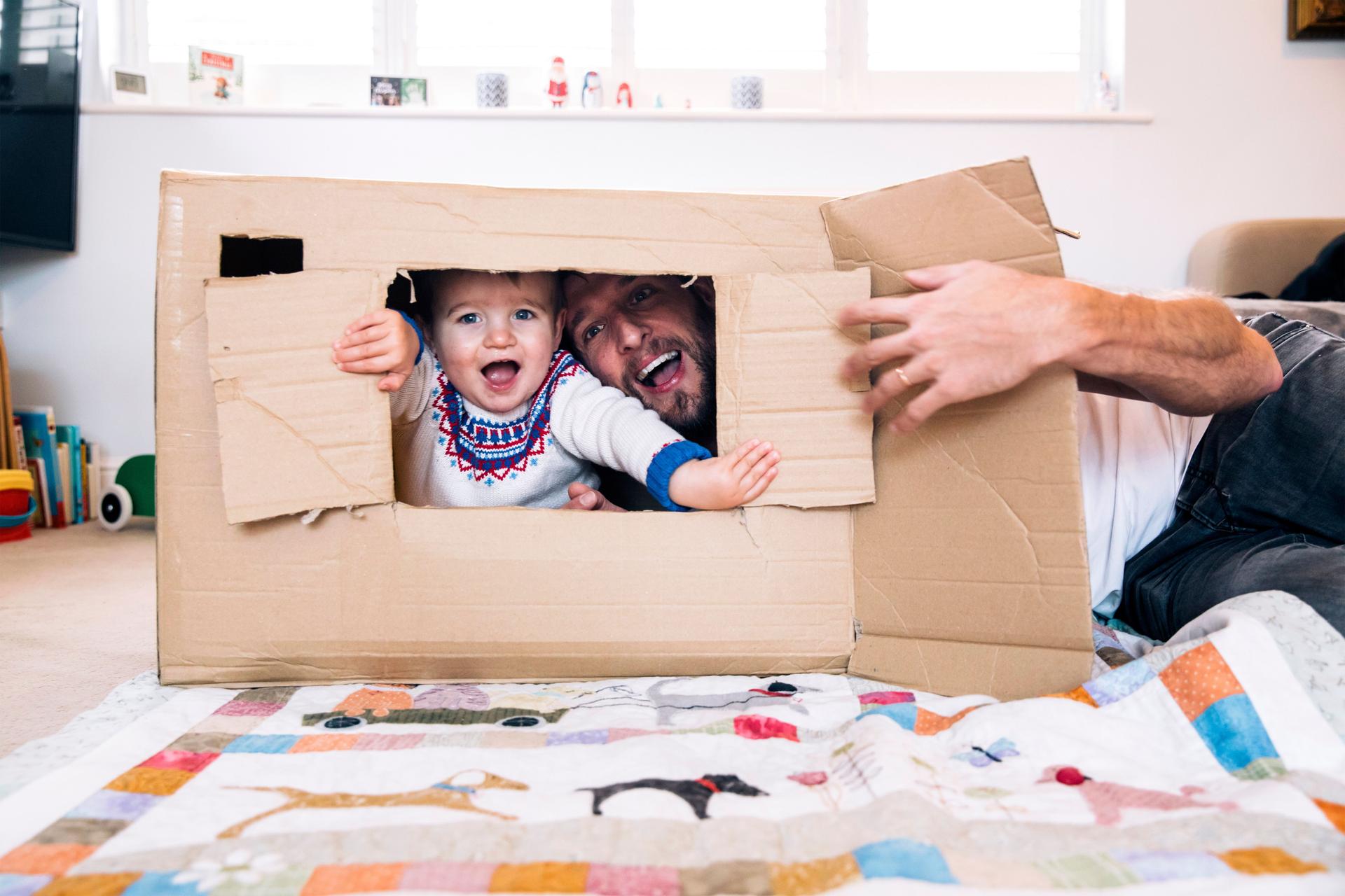 Vater und Kind spielen mit einem Karton als Haus im Kinderzimmer.