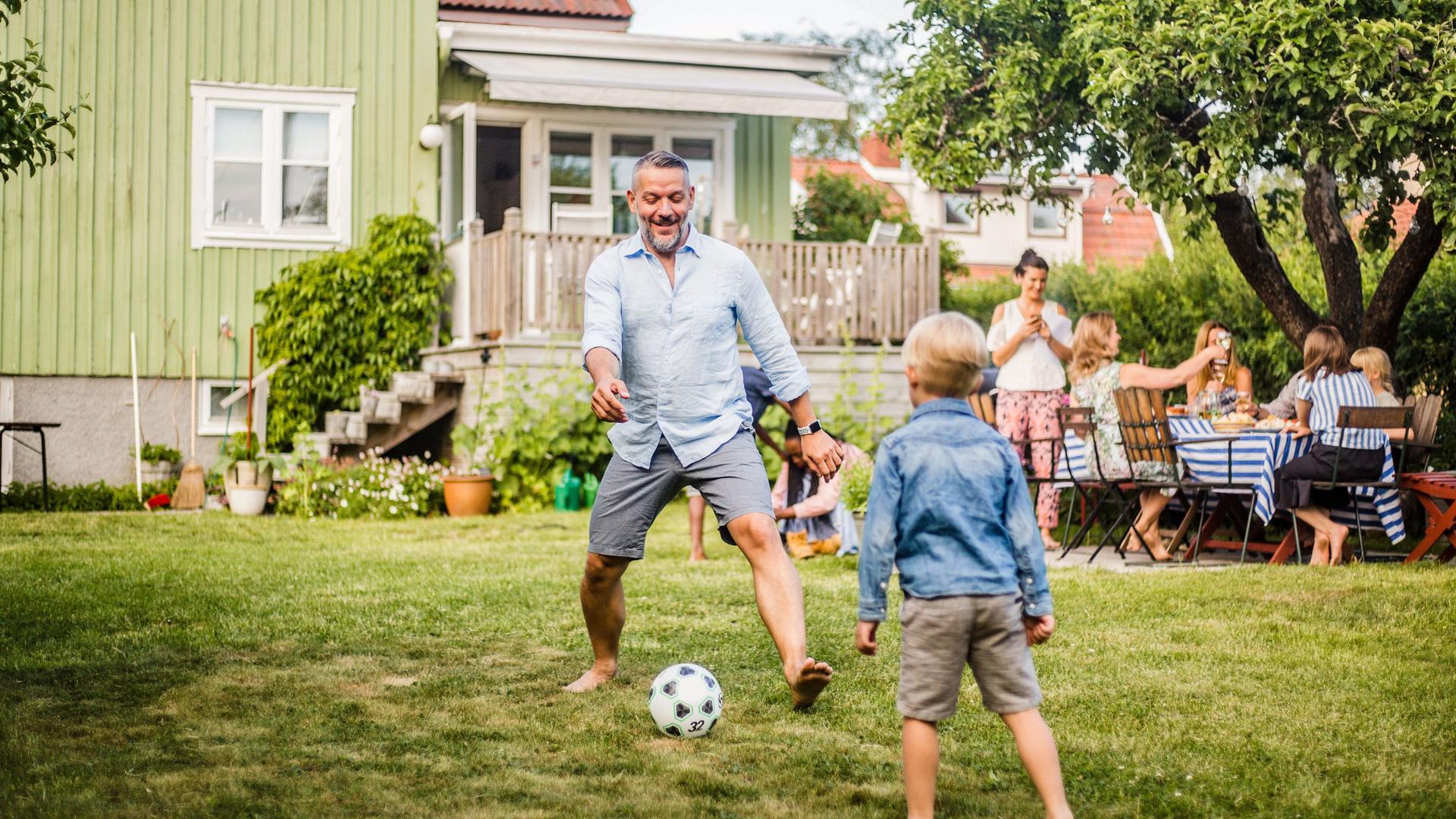 Ein Mann spielt im Garten mit seinem Sohn Fußball.