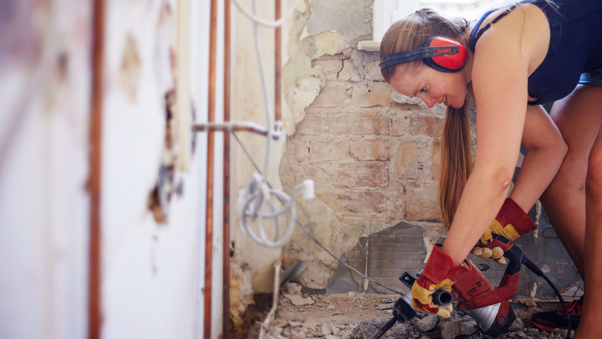 Frau mit Kopfhörern und Schlagbohrer arbeitet auf einer Baustelle