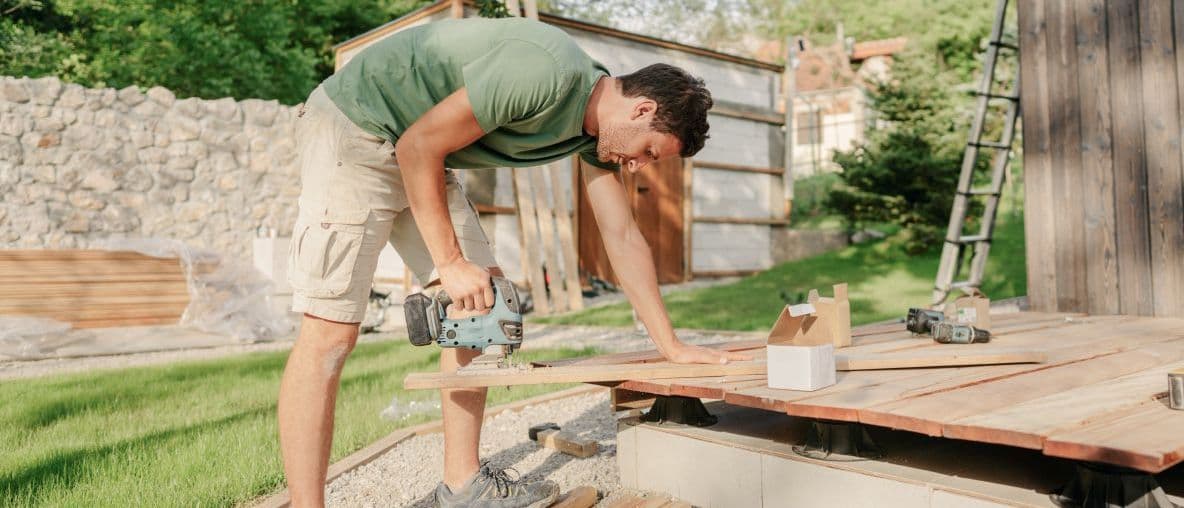 Mann sägt Holzbretter im Garten für eine Terrasse oder ein kleines Holzbauprojekt.