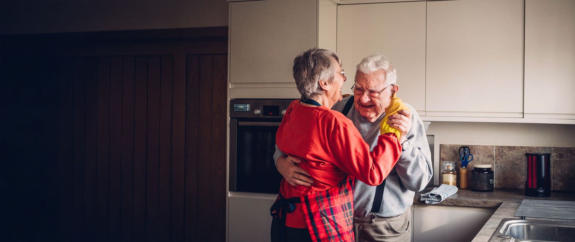 Älteres Paar tanzt lächelnd in einer hellen Küche