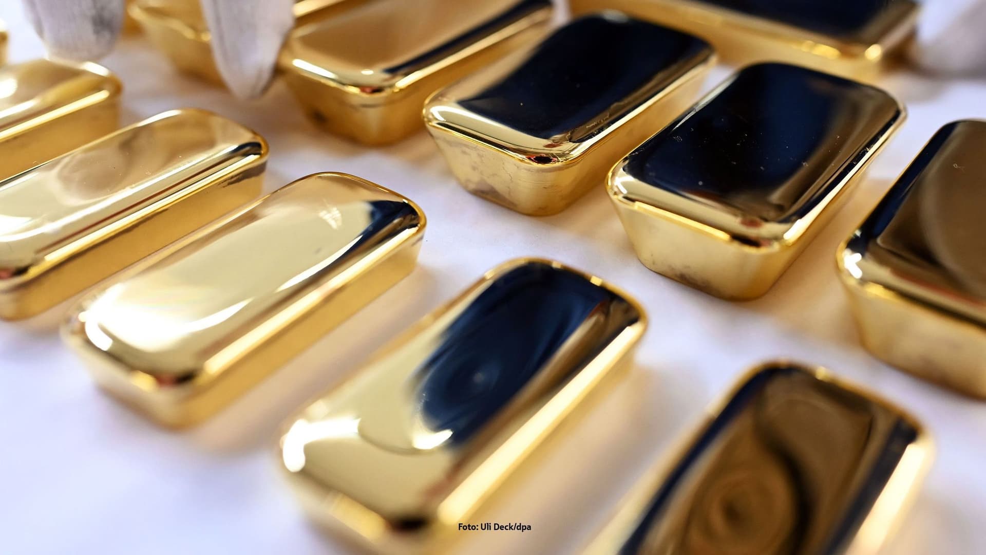 Eine Hand mit einem weißen Baumwollhandschuh sortiert Goldbarren.