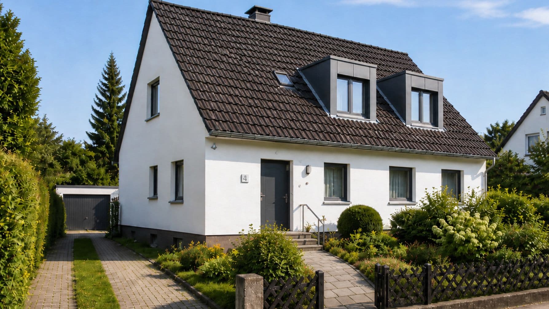 Einfamilienhaus mit gepflegtem Garten und zwei modernen Dachgauben auf einem steilen Ziegeldach.