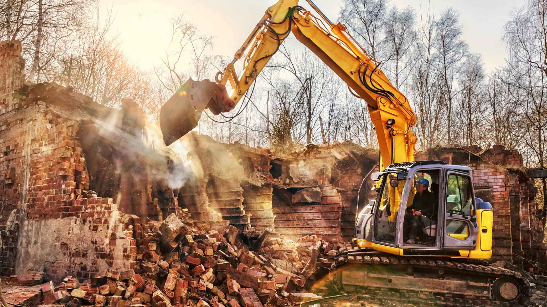 Baggerfahrer reißt mit einer Baggerschaufel die Wände eines Hauses ein.