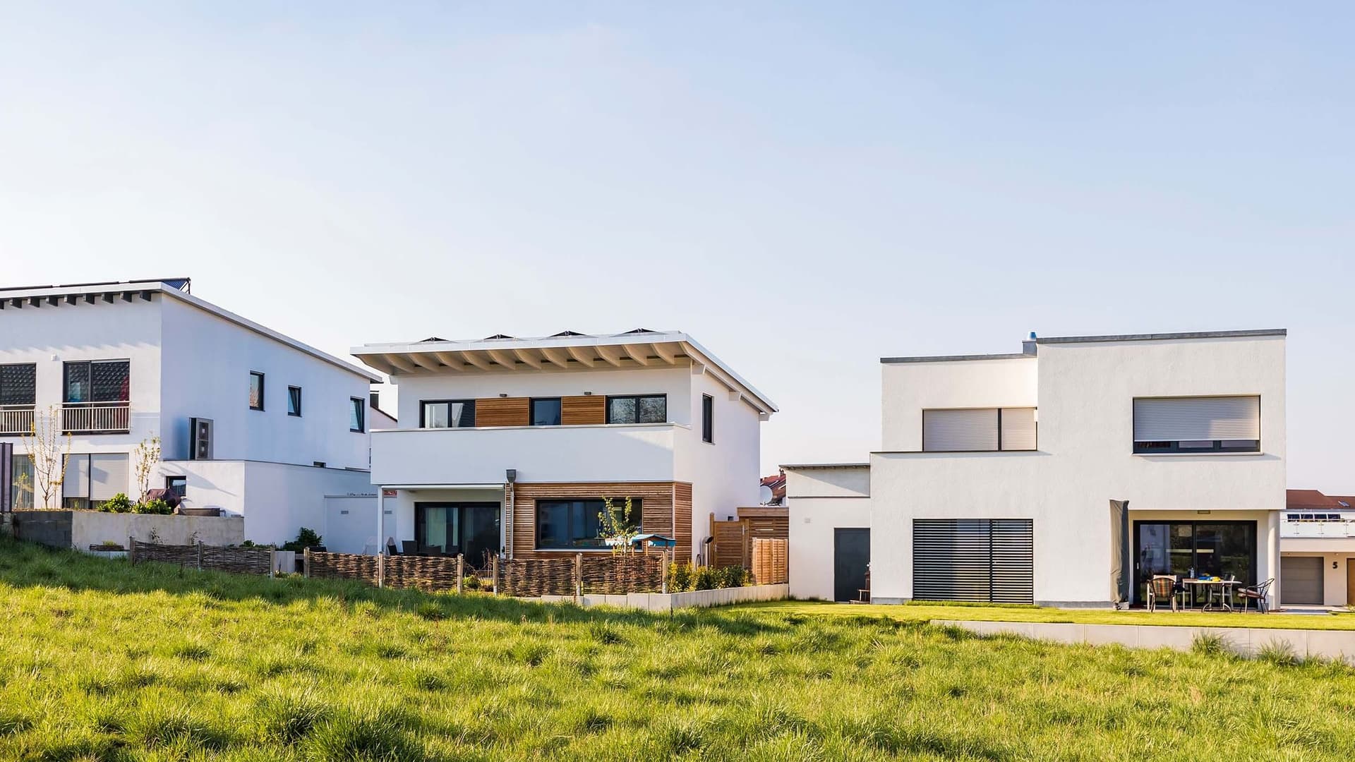 Moderne, weiße Häuser mit Flach-/Pultdächern und großen Fenstern stehen auf grünem Gras. Sie zeigen Energieeffizienz durch Solaranlagen.