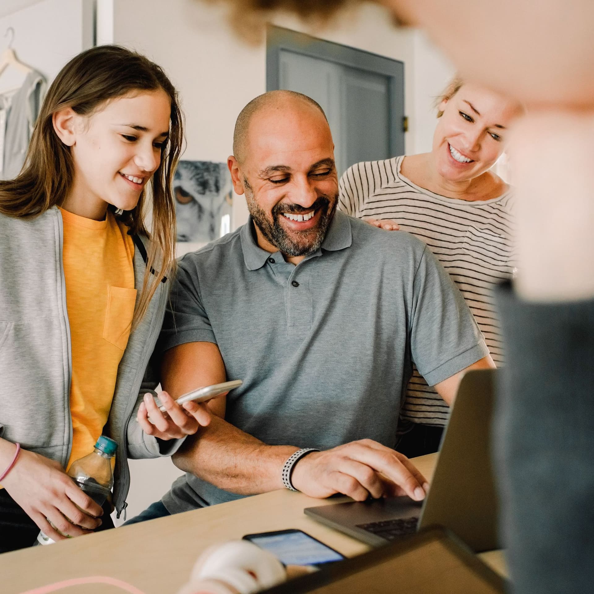 Eine Familie mit zwei Kindern im Teenageralter an einem Stehtisch. Sie lächeln und schauen auf einen Laptop, den der Vater vor sich hat.