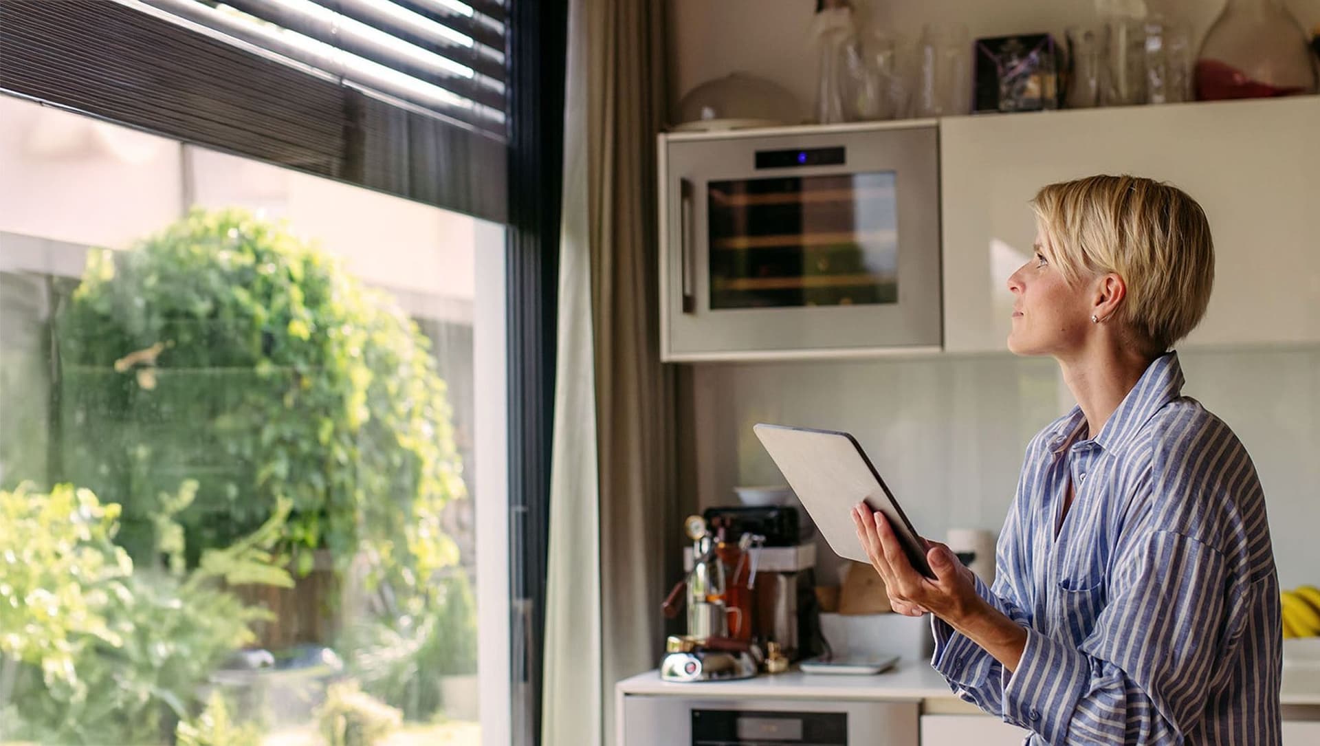 Eine Frau bedient elektrische Rollläden in einem modernen Wohnraum. Sie steht vor einem Fenster und zieht an einem Schalter, während die Rollläden sanft nach unten fahren.
