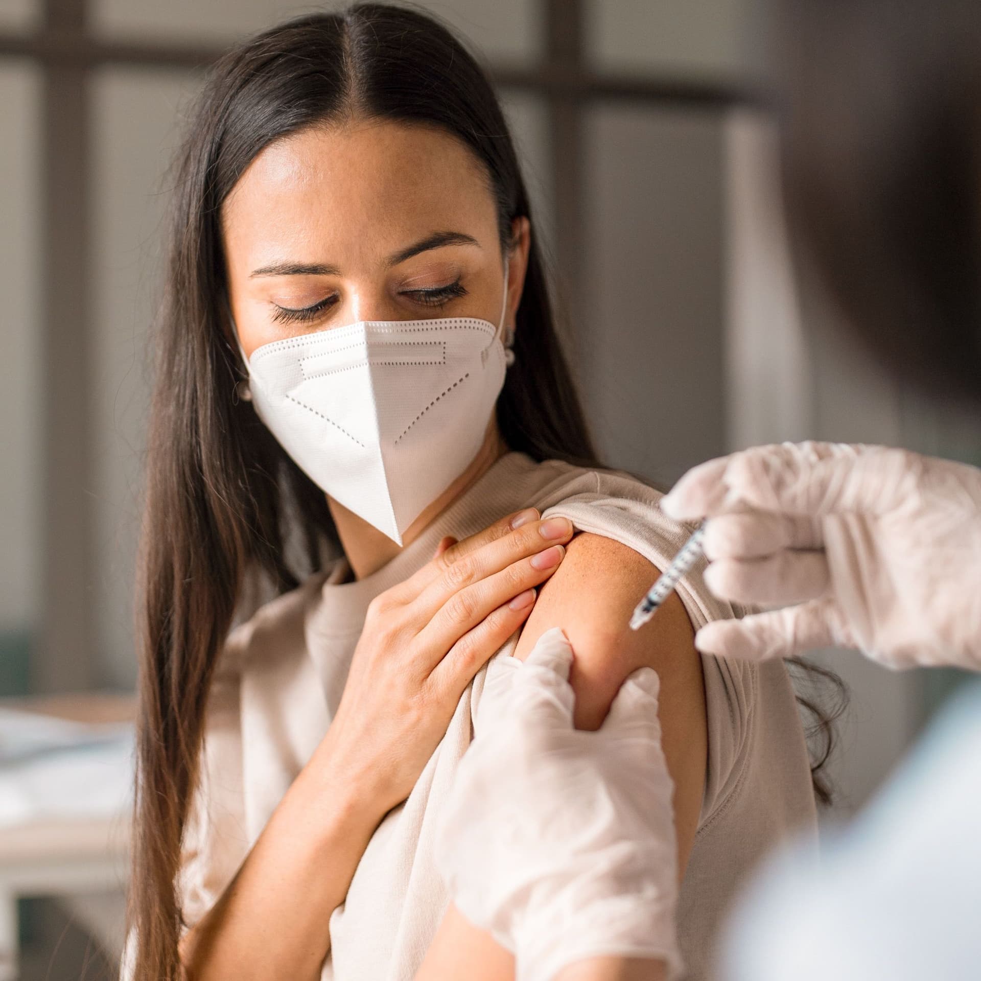 Frau mit Maske bekommt eine Spritze in den Arm