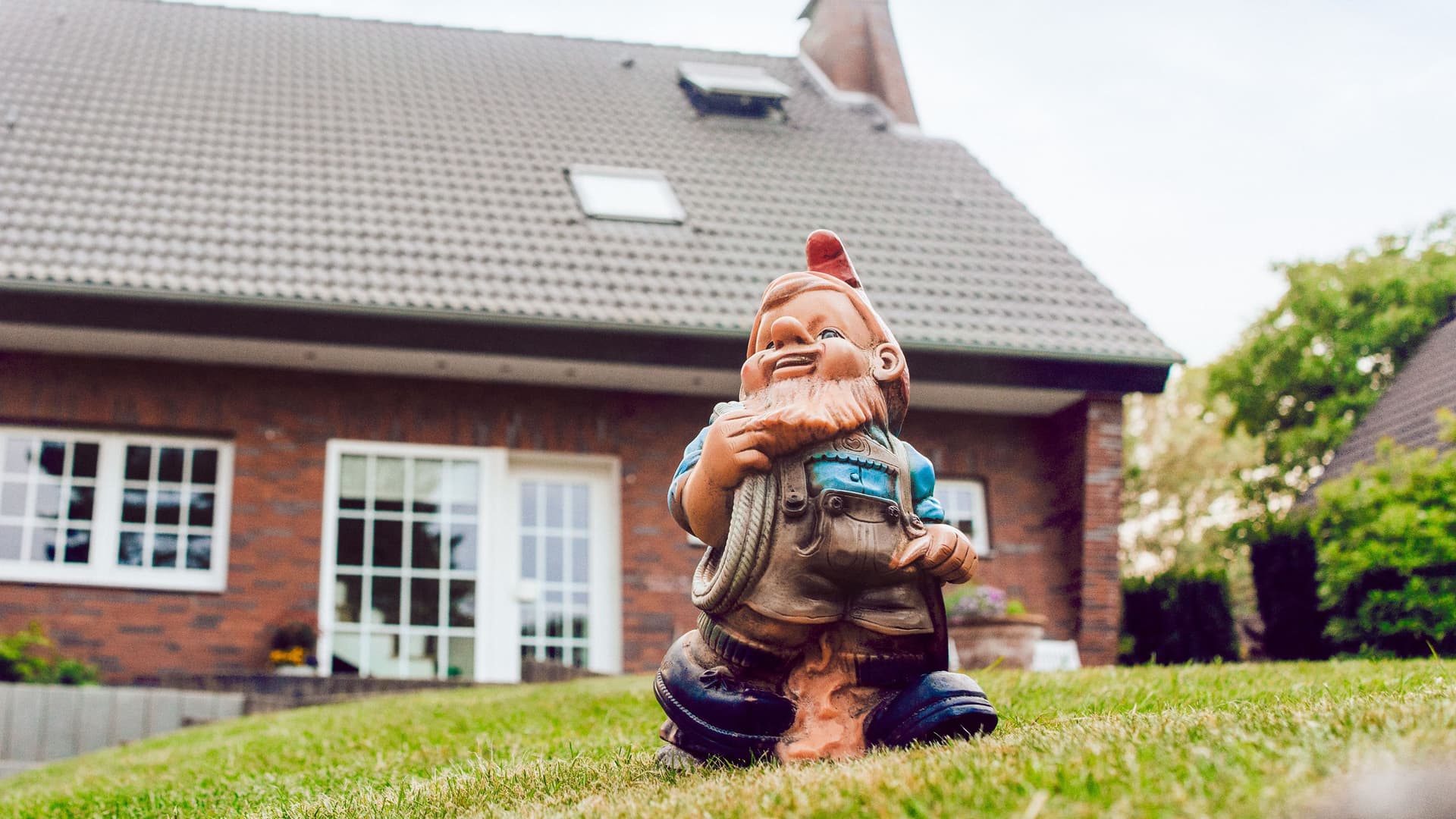 Aufnahme eines Gartenzwergs, der auf einer grünen Wiese vor einem Einfamilienhaus steht.