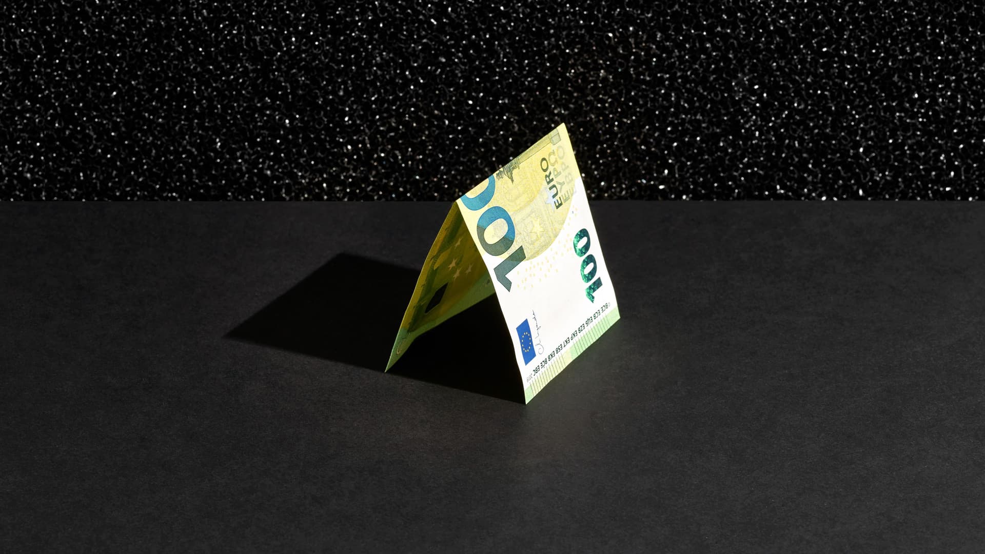 Ein 100-Euro Schein liegt gefaltet auf einem schwarzem Hintergrund.