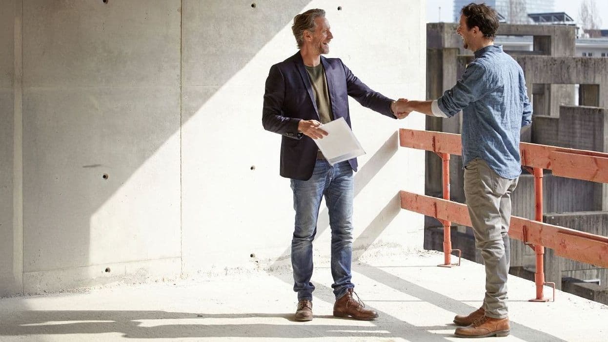 zwei männer geben sich auf einer baustelle die hand