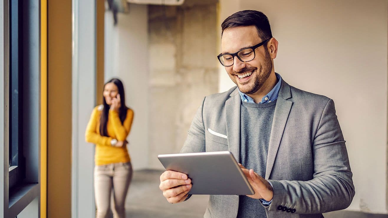 Mann mit Brille und Tablet in modernem Bürogebäude Frau telefoniert im Hintergrund in leerem Innenraum