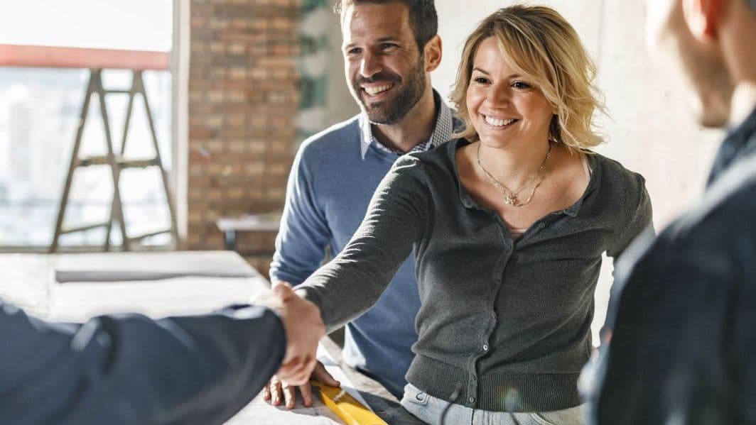freundliches paar beim händeschütteln mit einer beratenden person in einer hellen wohnung