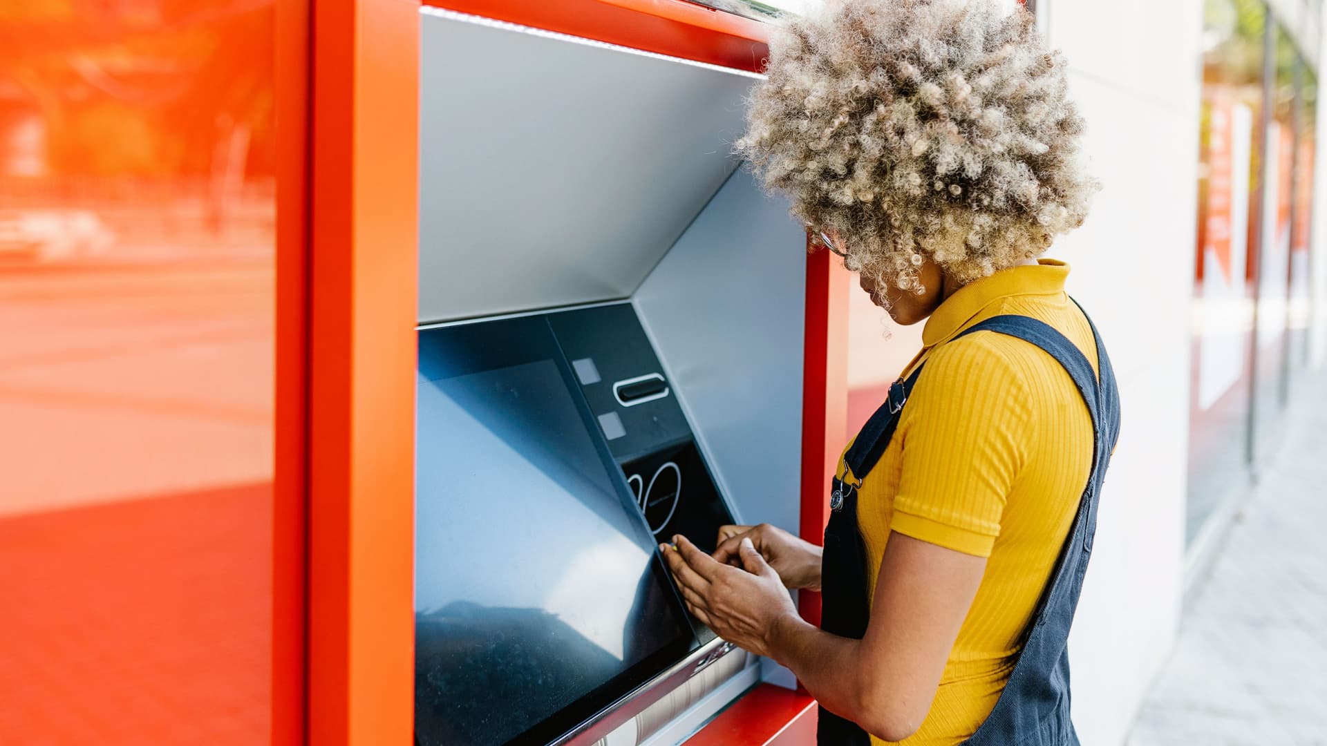 Junge Frau mit Afro hebt an einem Bankautomat Geld ab